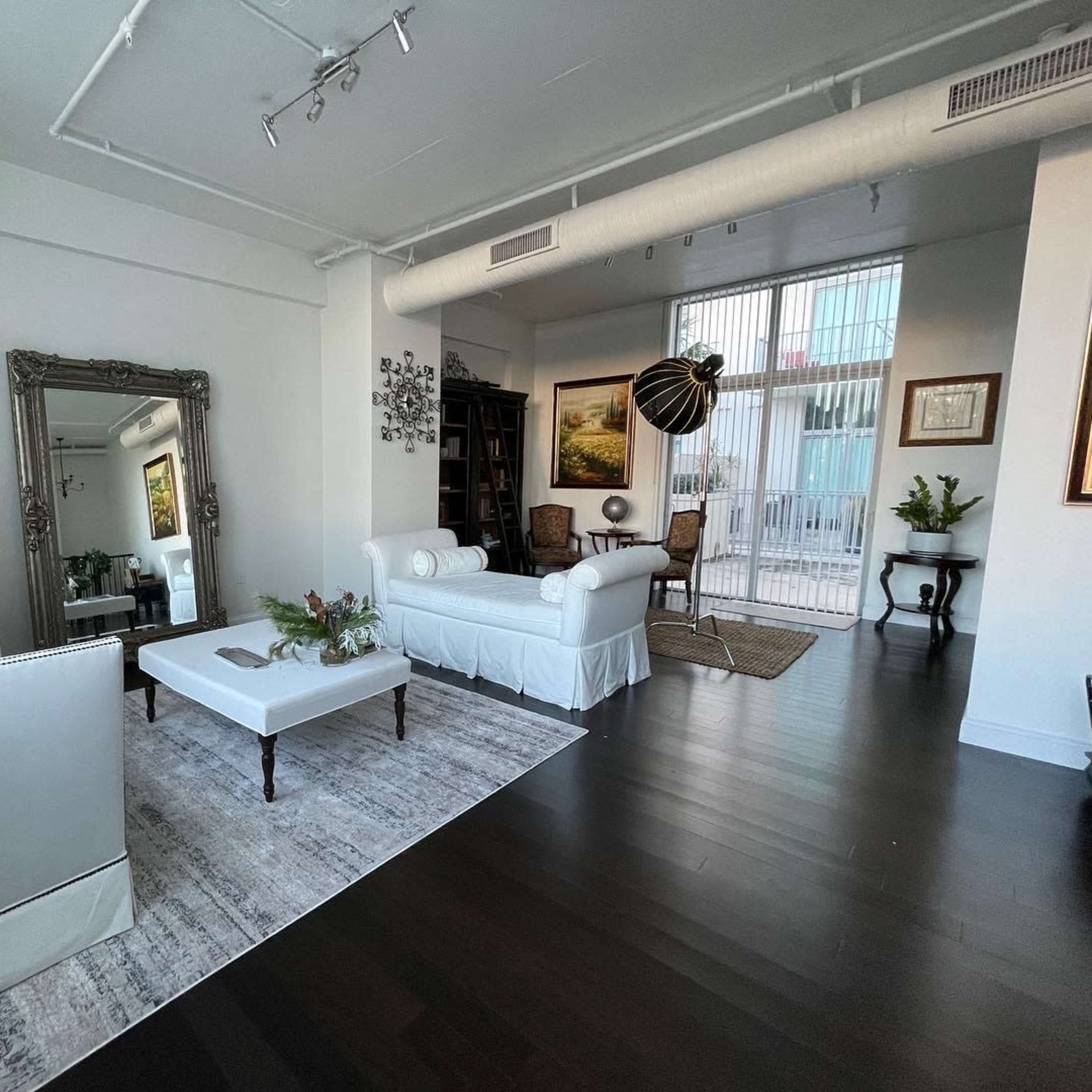 A contemporary living room with a white sofa, a coffee table with flowers, and large windows revealing an outdoor balcony.