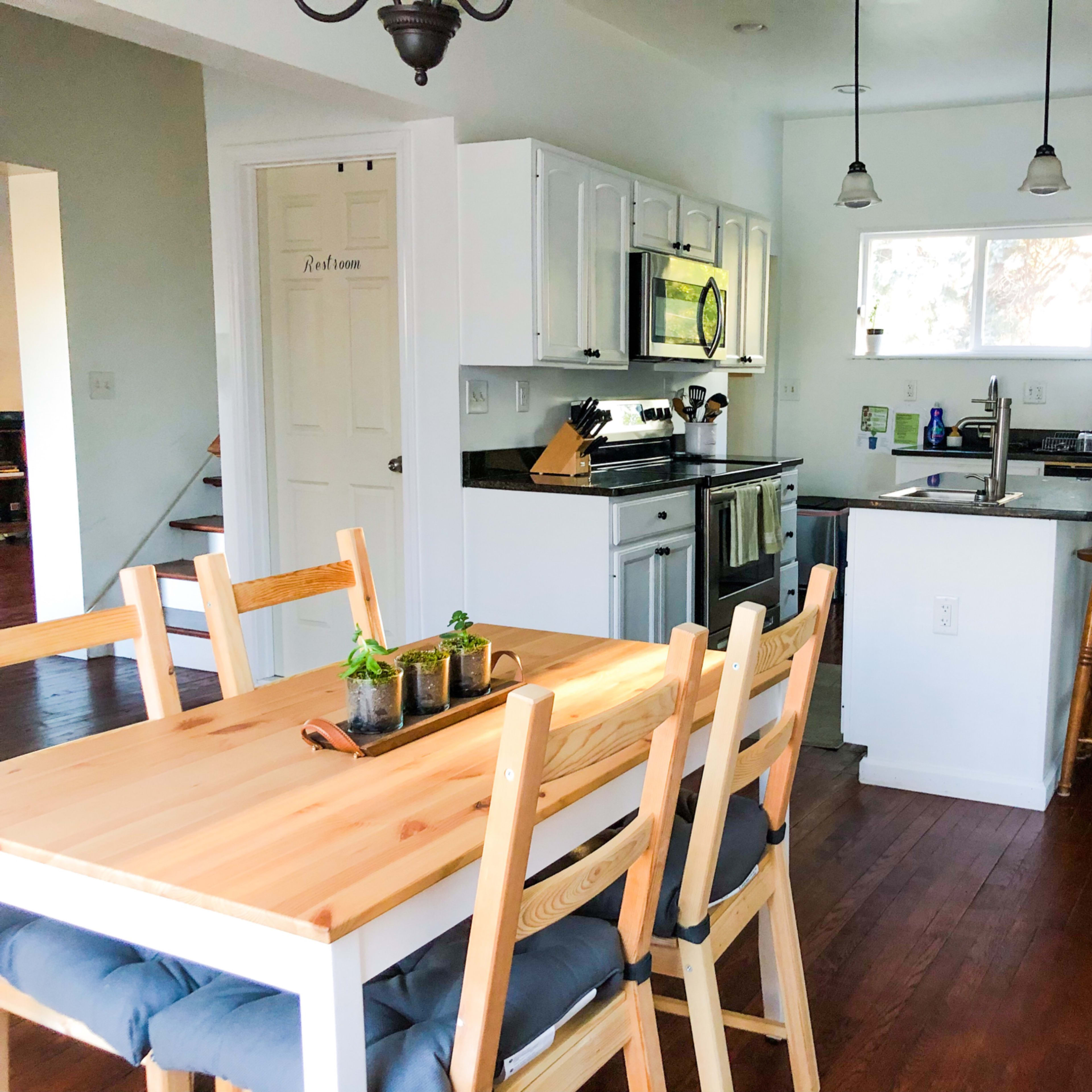 A modern kitchen features white cabinetry, stainless steel appliances, a wooden dining table, and hardwood floors.