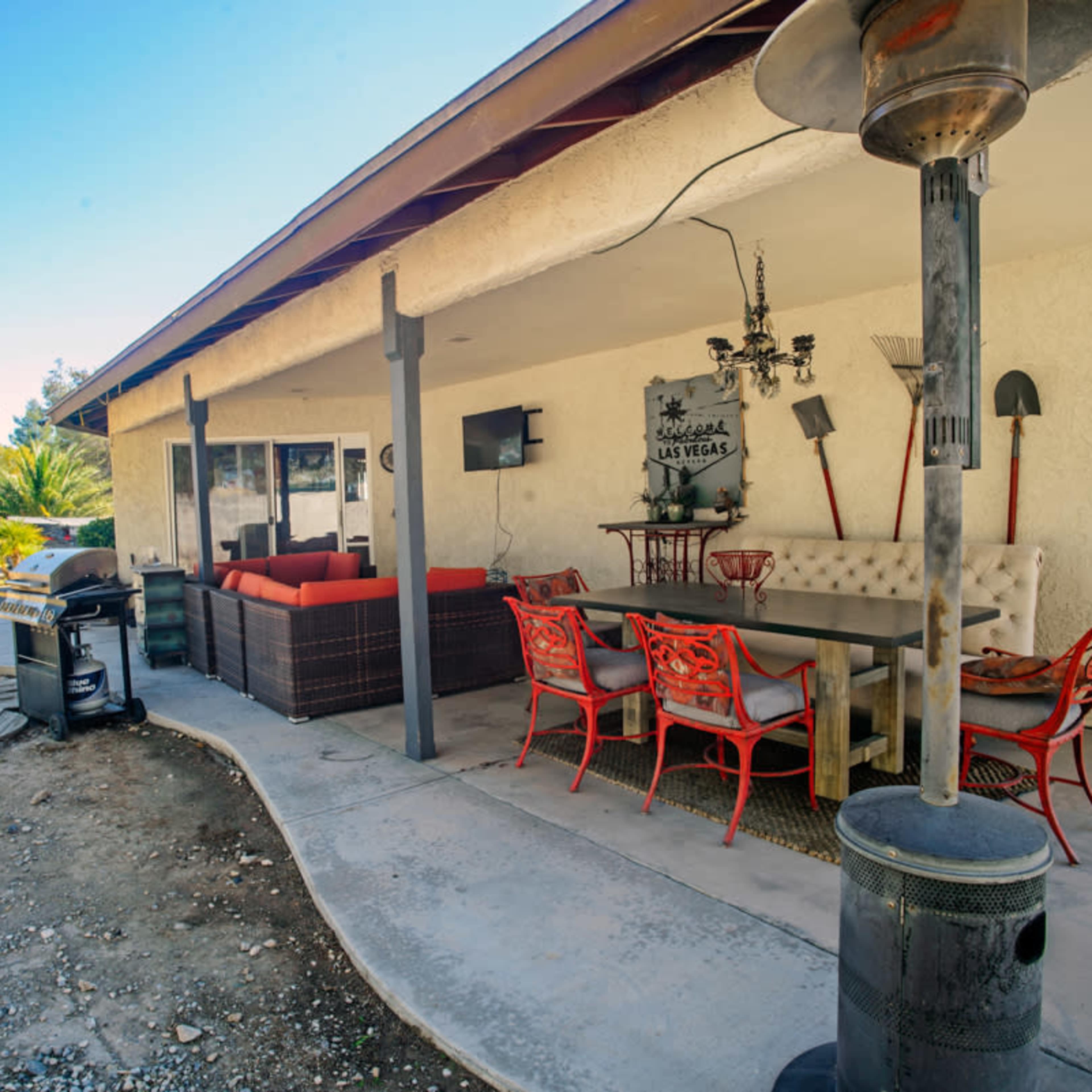A patio area with a seating arrangement, a dining table, barbecue grill, and a heater beside a house.