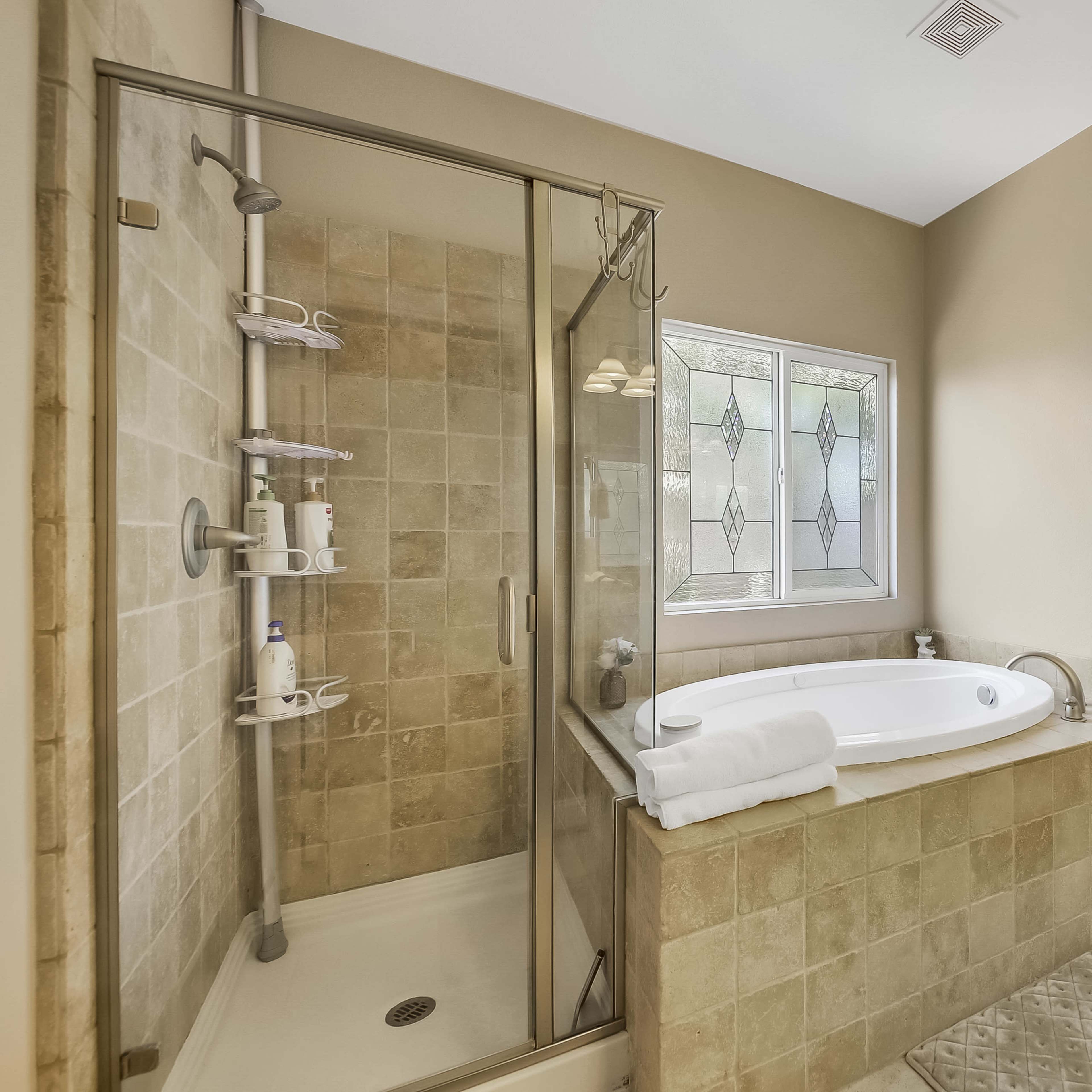 A spacious bathroom featuring a glass-enclosed shower, a freestanding bathtub, and a doorway leading to a bedroom.