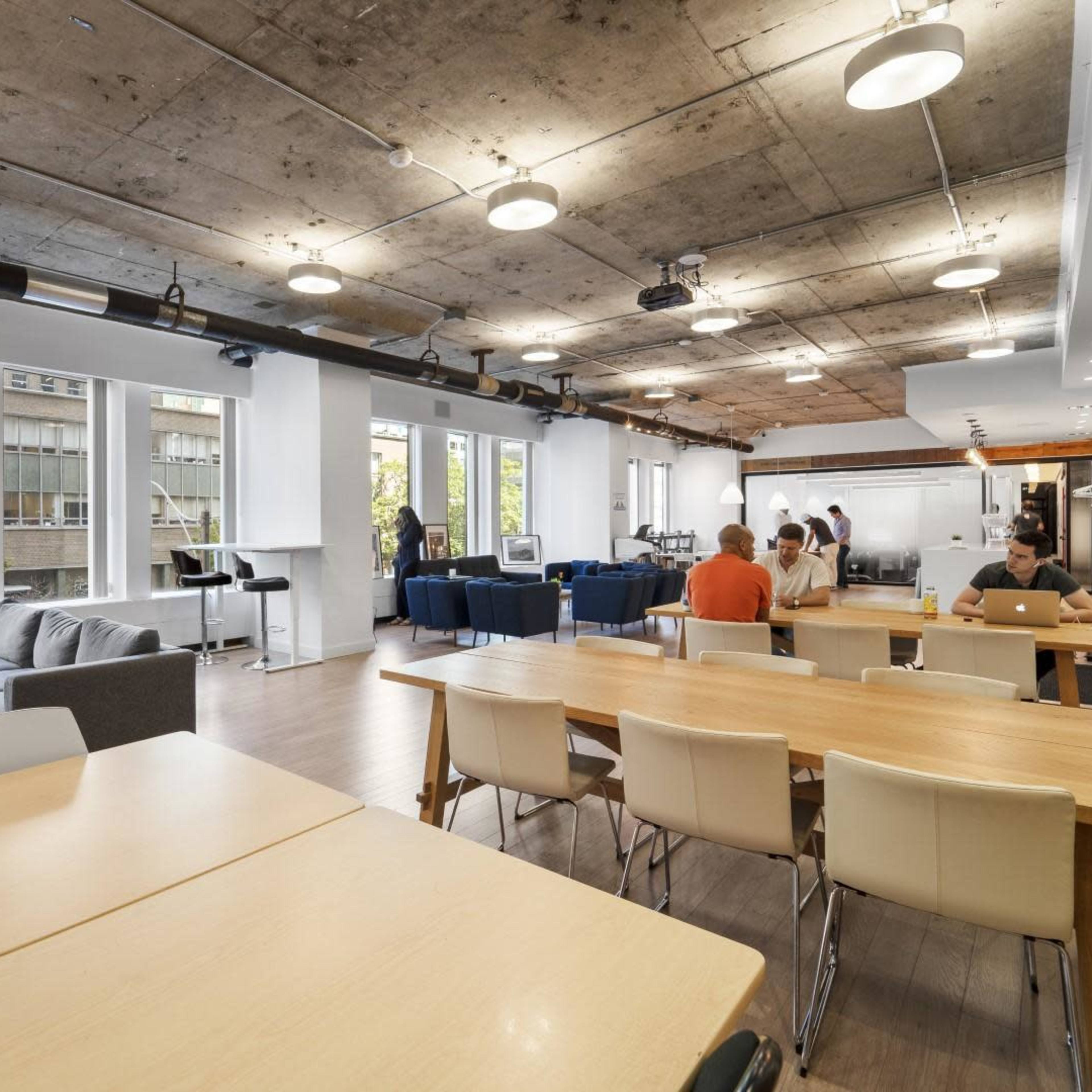 A spacious modern office with tables, a gray sofa, and people working in various activities.