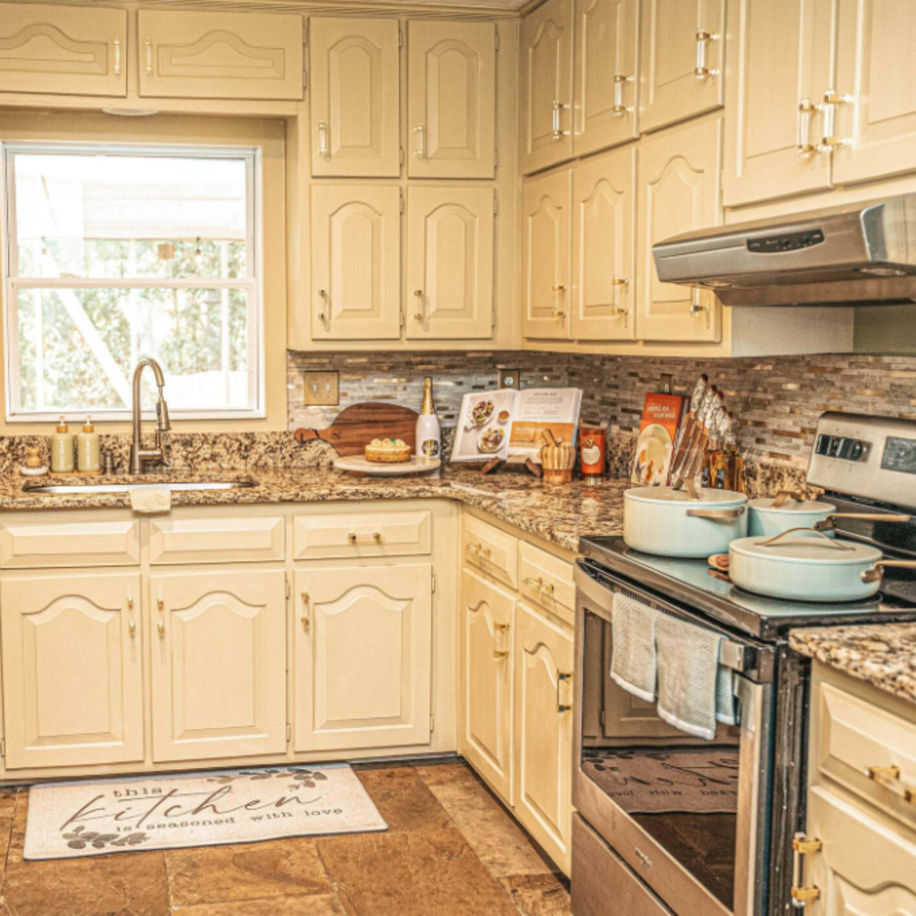 A kitchen with cream-colored cabinets, granite countertops, and stainless steel appliances, featuring a window providing natural light.