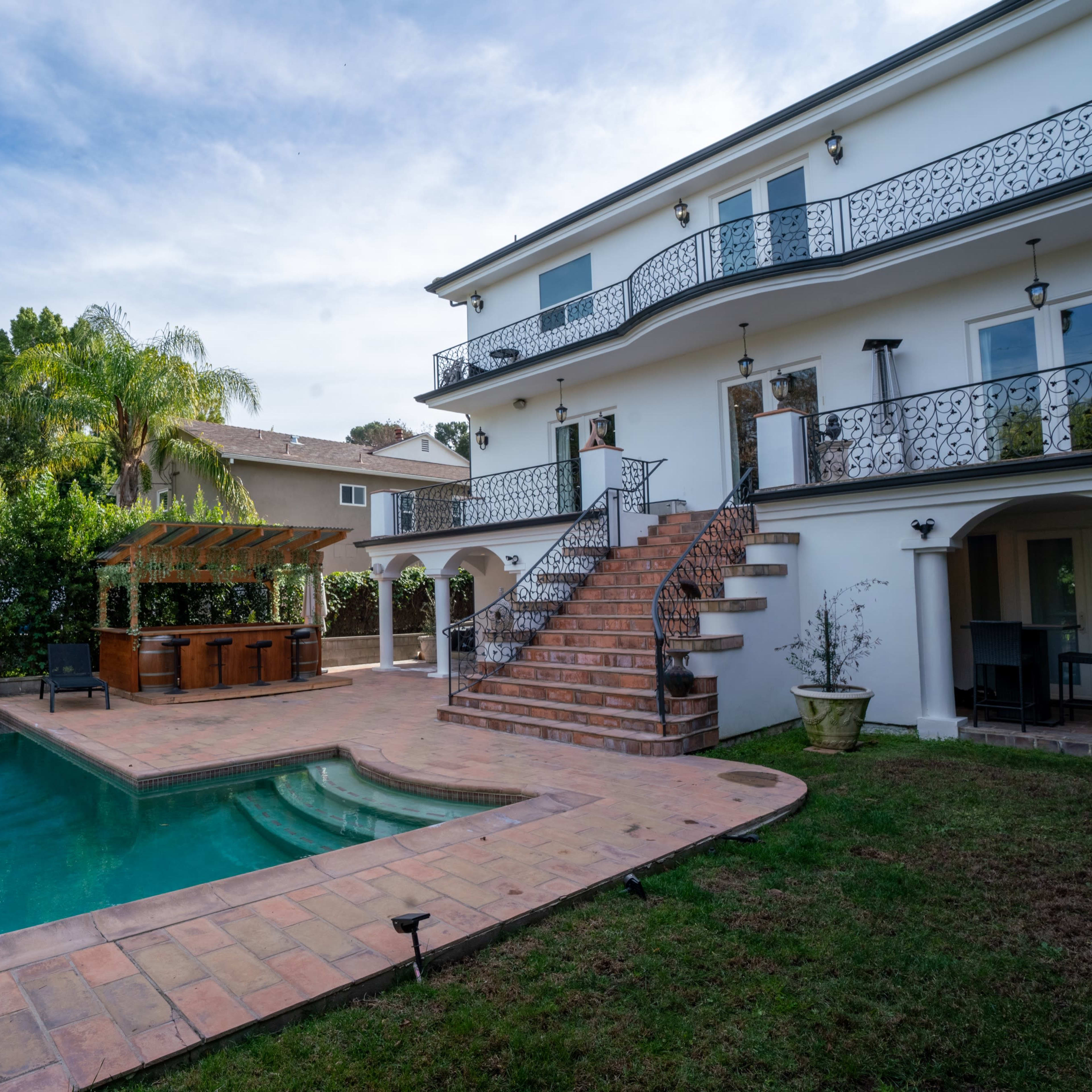A two-story house with a swimming pool and a landscaped backyard, featuring a staircase leading to a balcony.