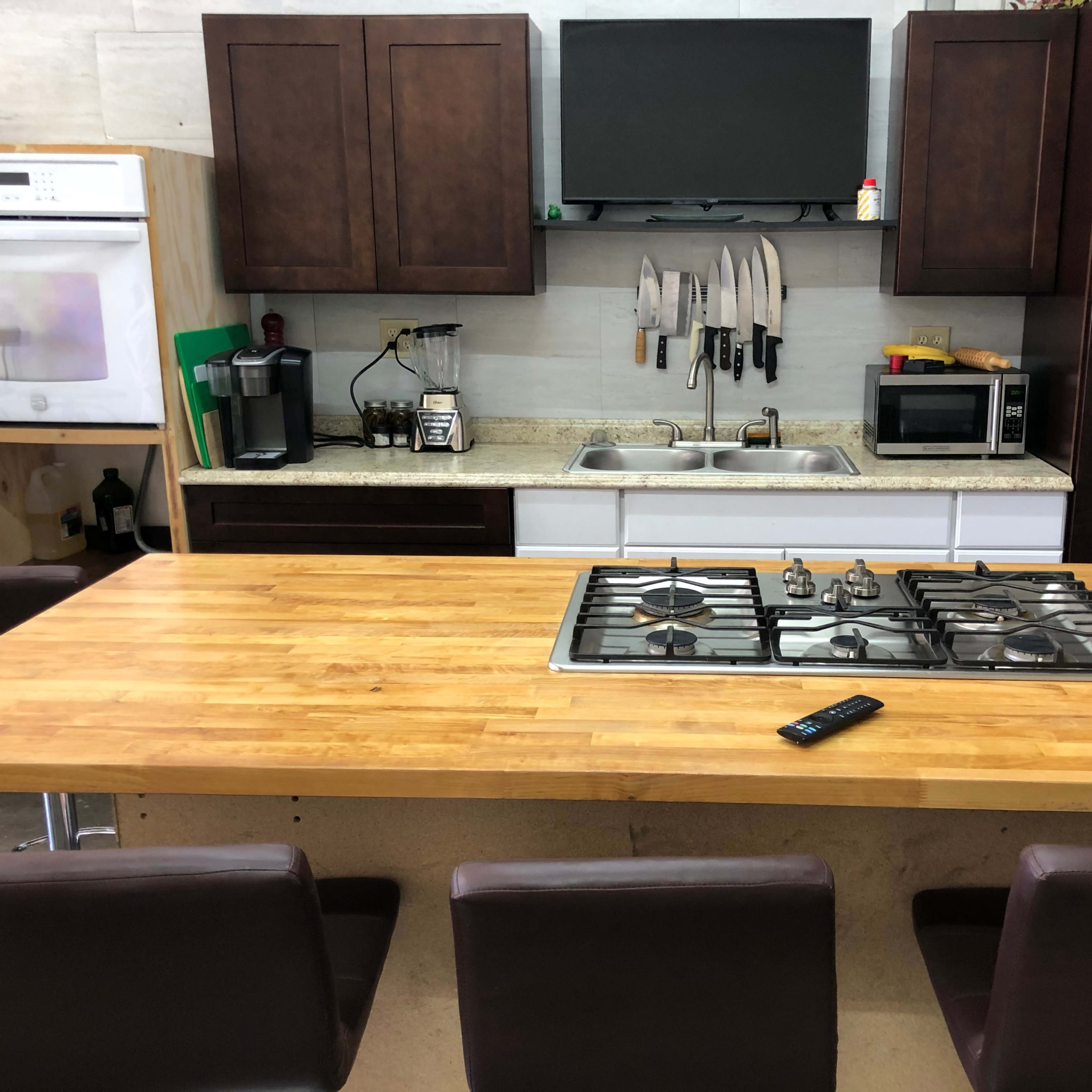A kitchen with dark cabinetry, a countertop with a built-in gas stove, and a central wooden table surrounded by four brown chairs.