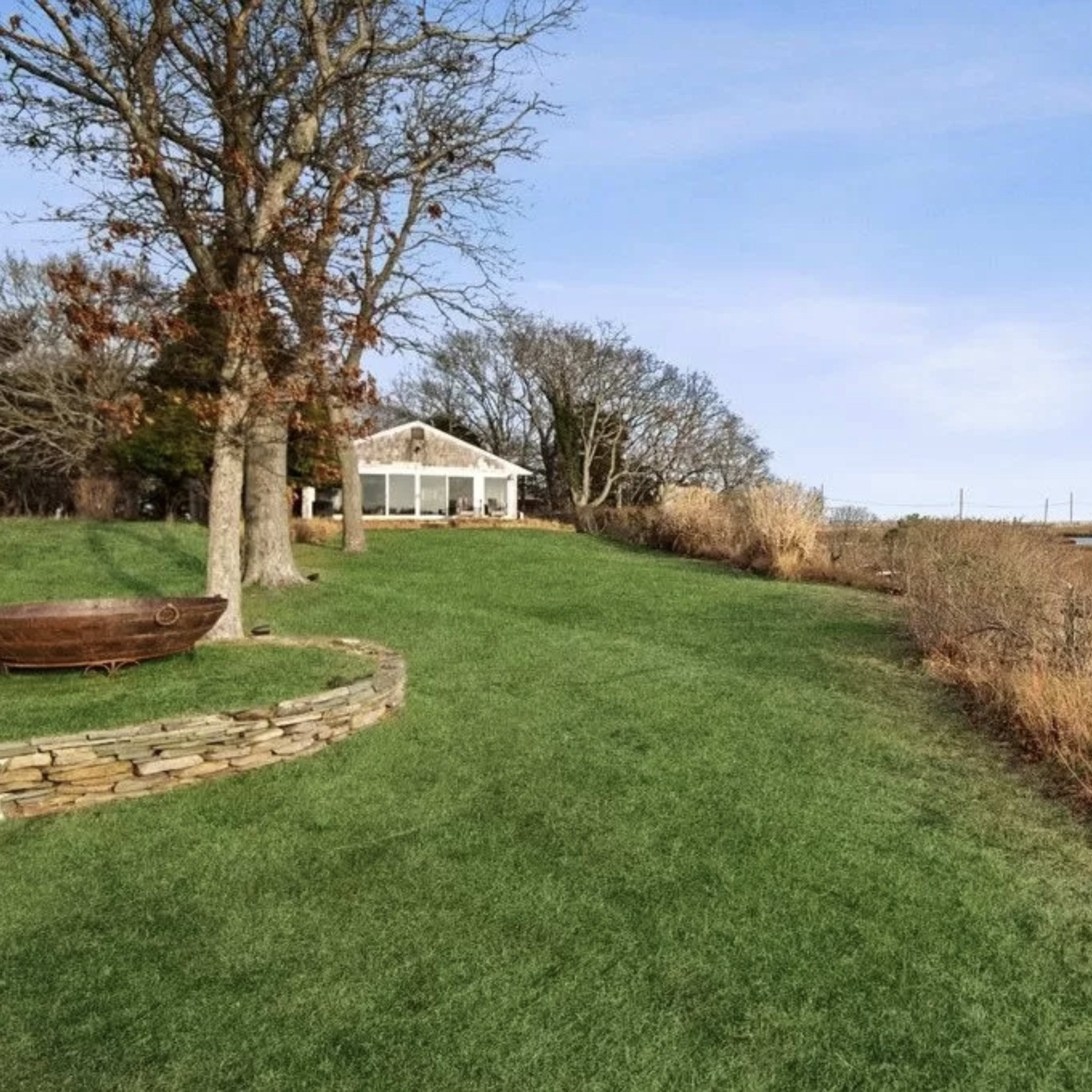 A grassy yard with a stone border leading to a waterway, with a house and trees in the background.