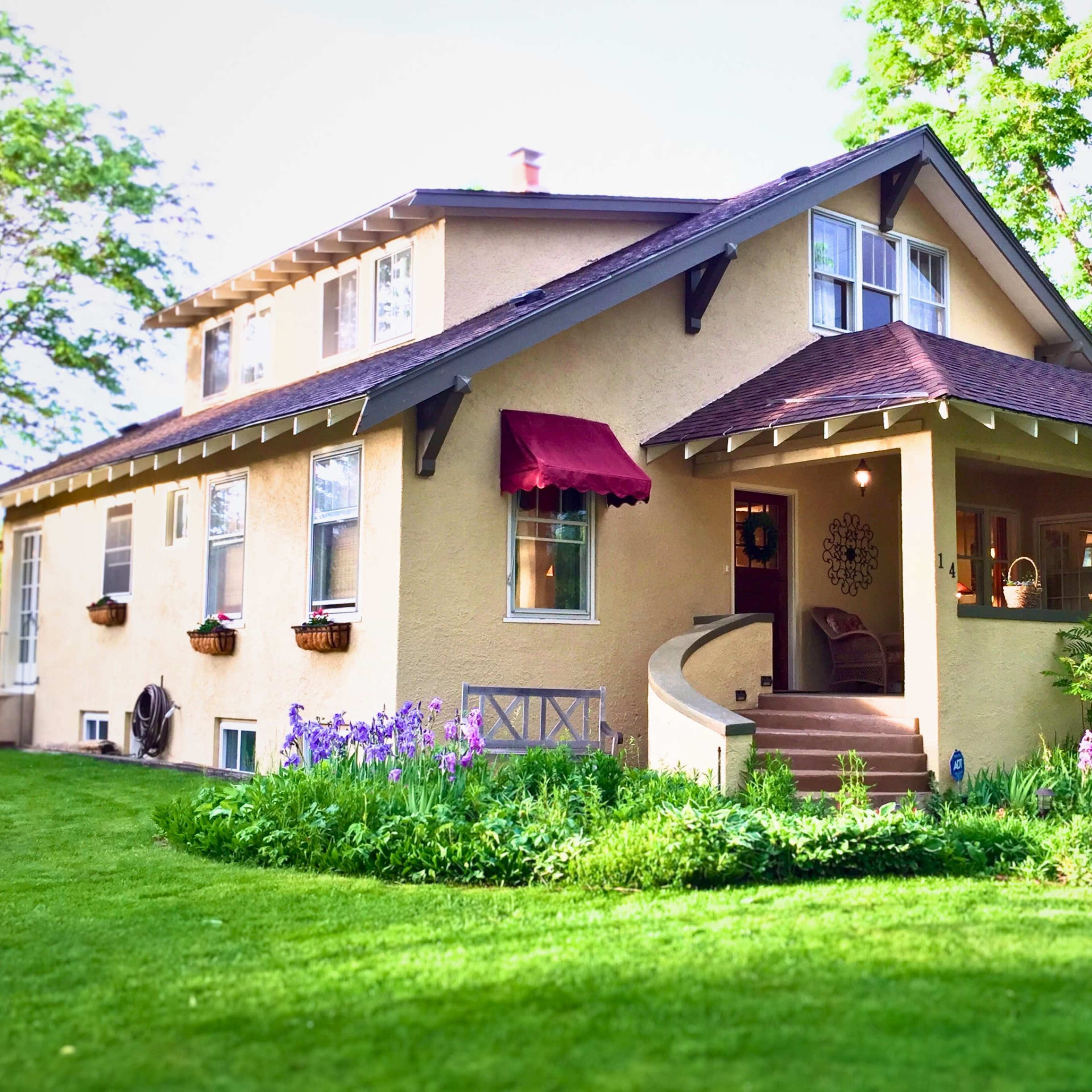 A two-story house with a sloped roof, a covered porch, and colorful flower beds surrounded by a well-maintained lawn.