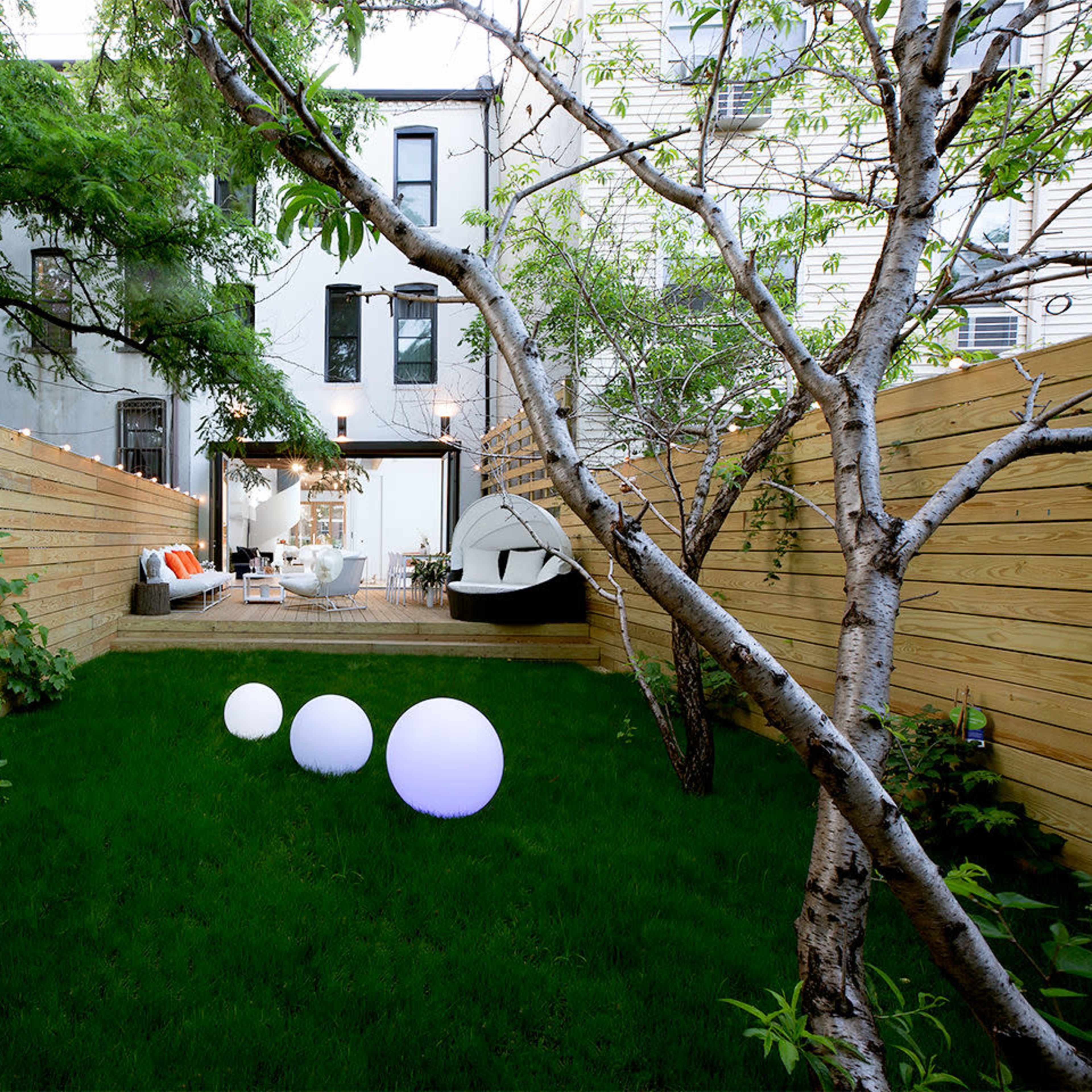 A well-maintained backyard features a green lawn, wooden fencing, and decorative light orbs, leading to a modern home with large windows.