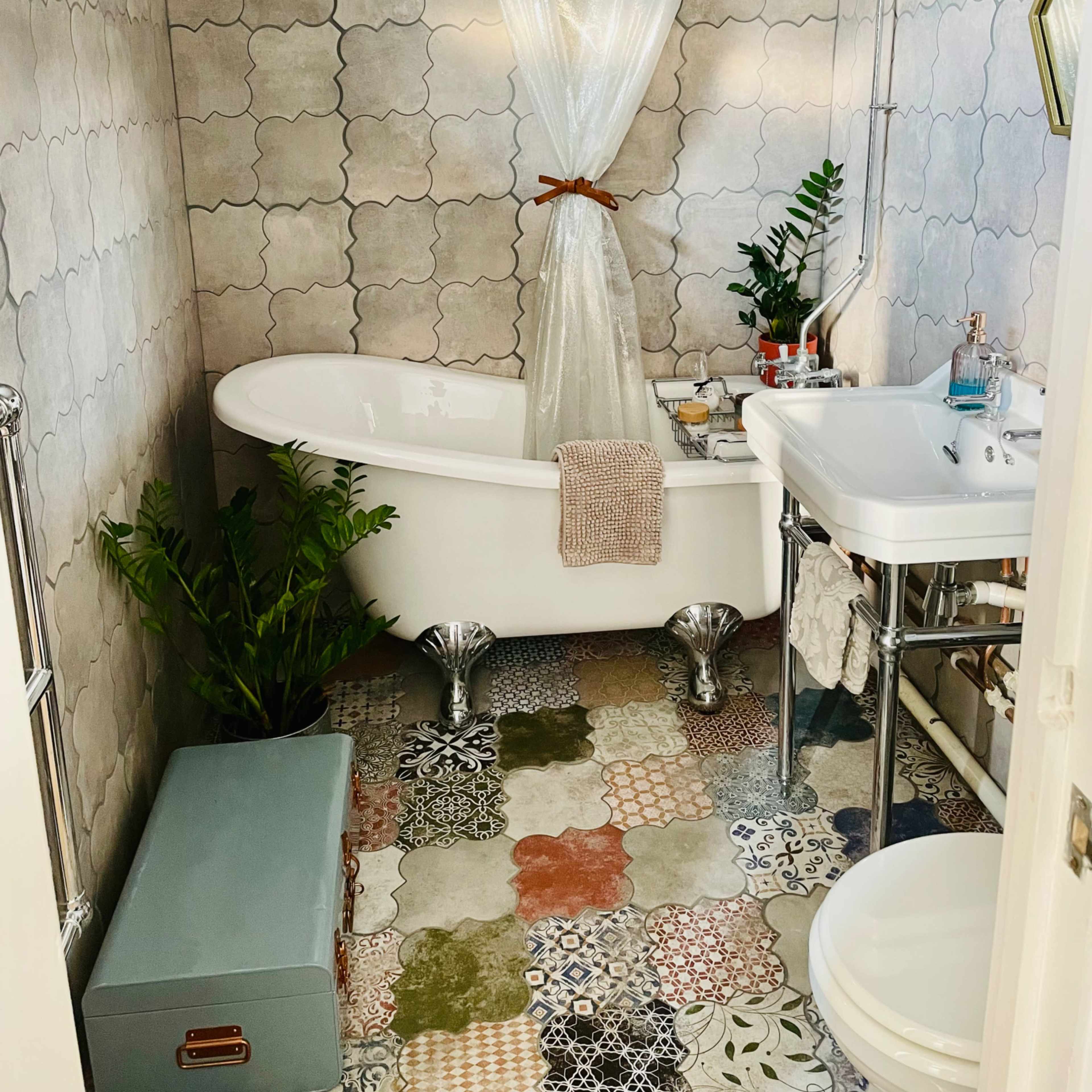 A stylish bathroom featuring a freestanding bathtub with a shower curtain, a sink on a metal stand, and a variety of patterned tiles on the floor.