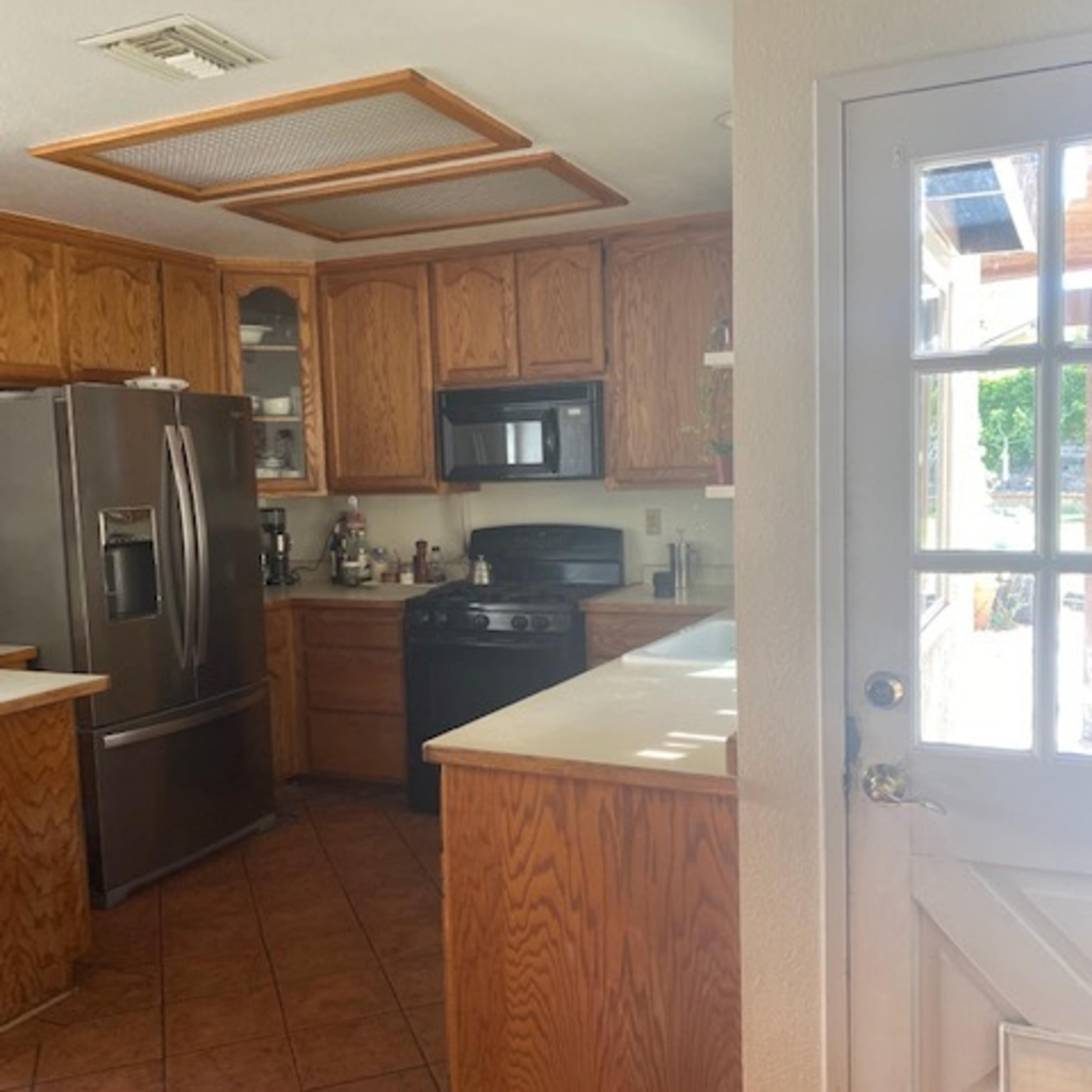A kitchen with wooden cabinets, a stainless steel refrigerator, and a door leading outside.