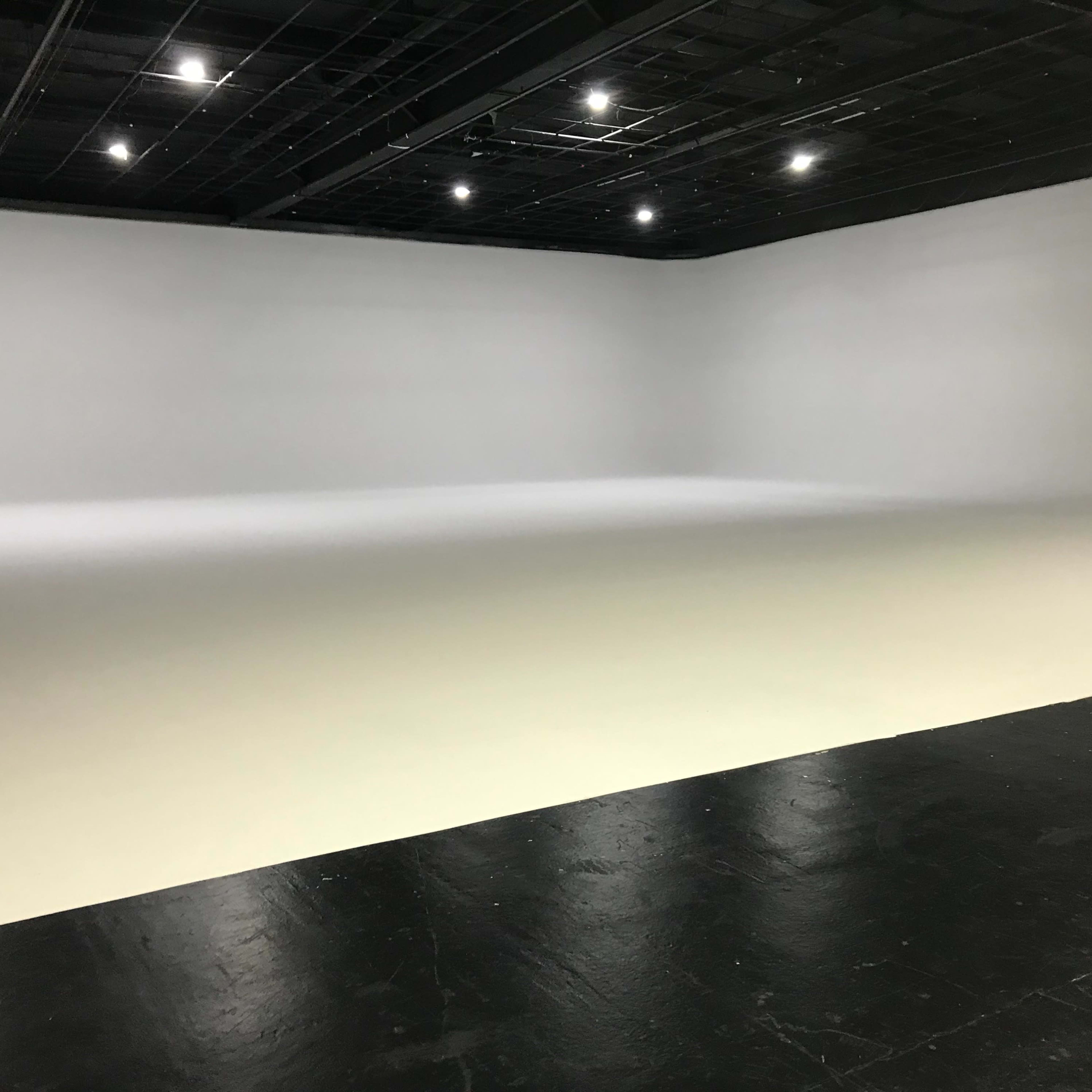 A large empty studio space with a seamless white backdrop and a black floor.