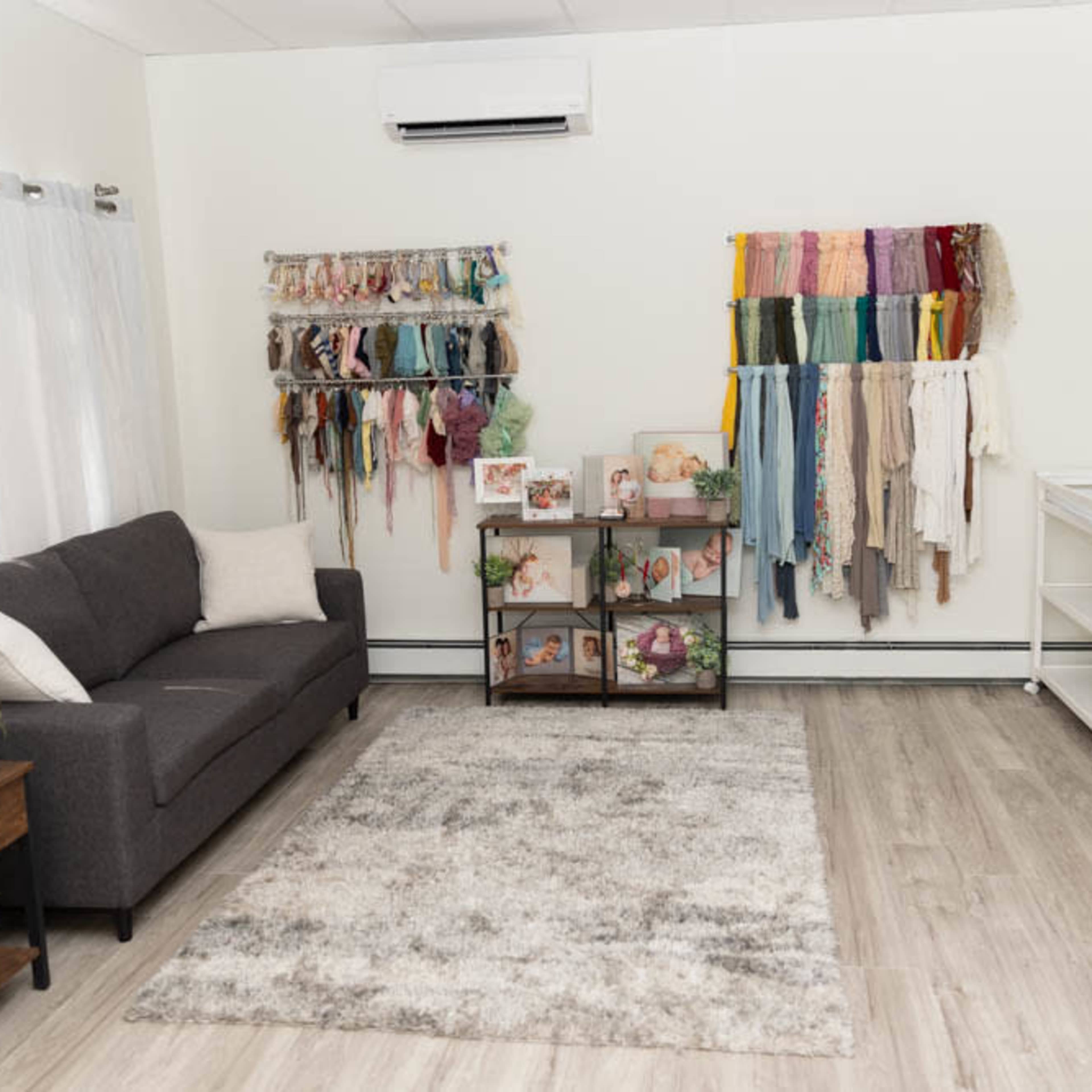A well-organized room featuring a gray sofa, a rug, and colorful fabric hangings on the walls, along with shelves displaying framed pictures and various items.