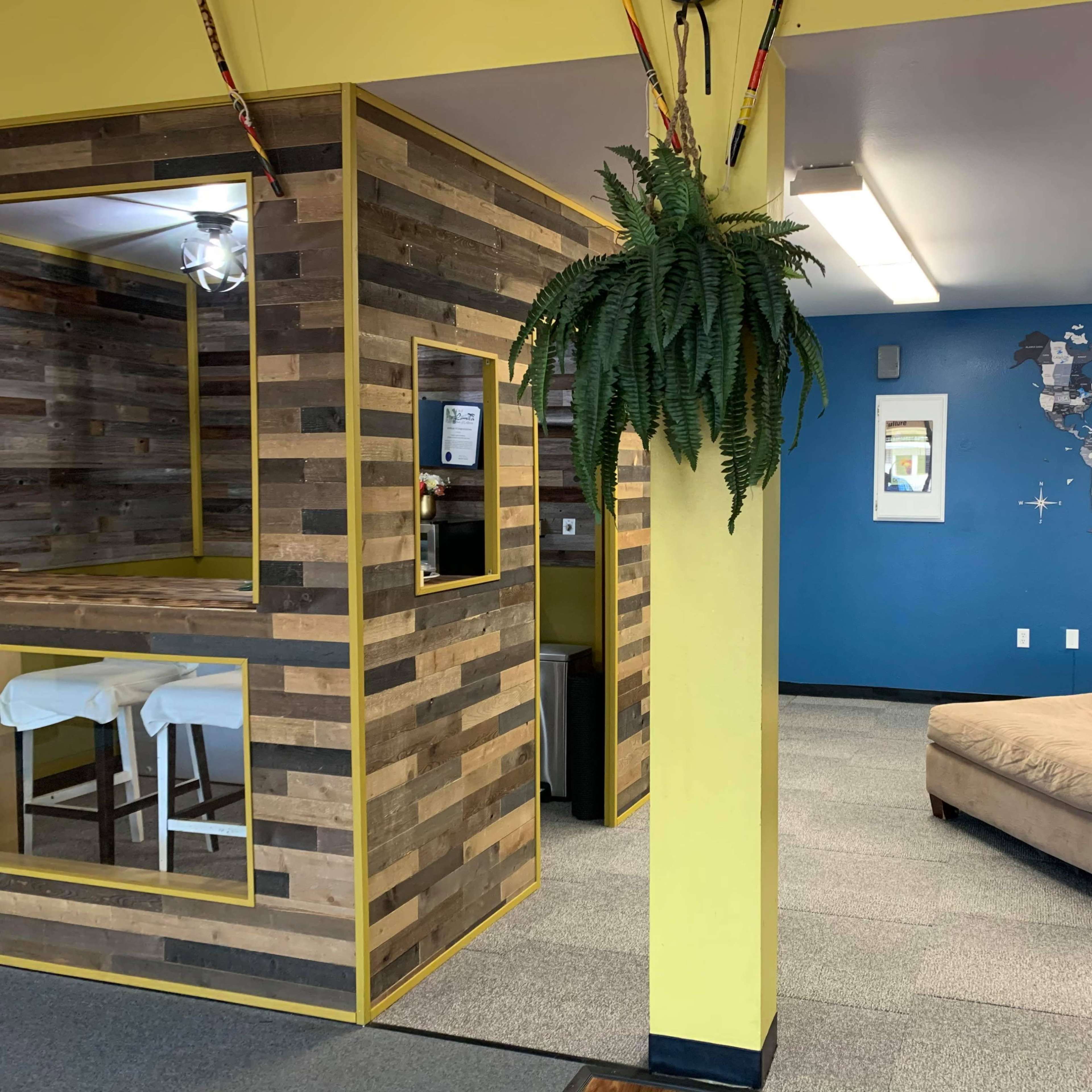 A room divided into two areas: one features a wooden accent wall with a small seating area, while the other has a large, beige couch and a blue wall with a world map.