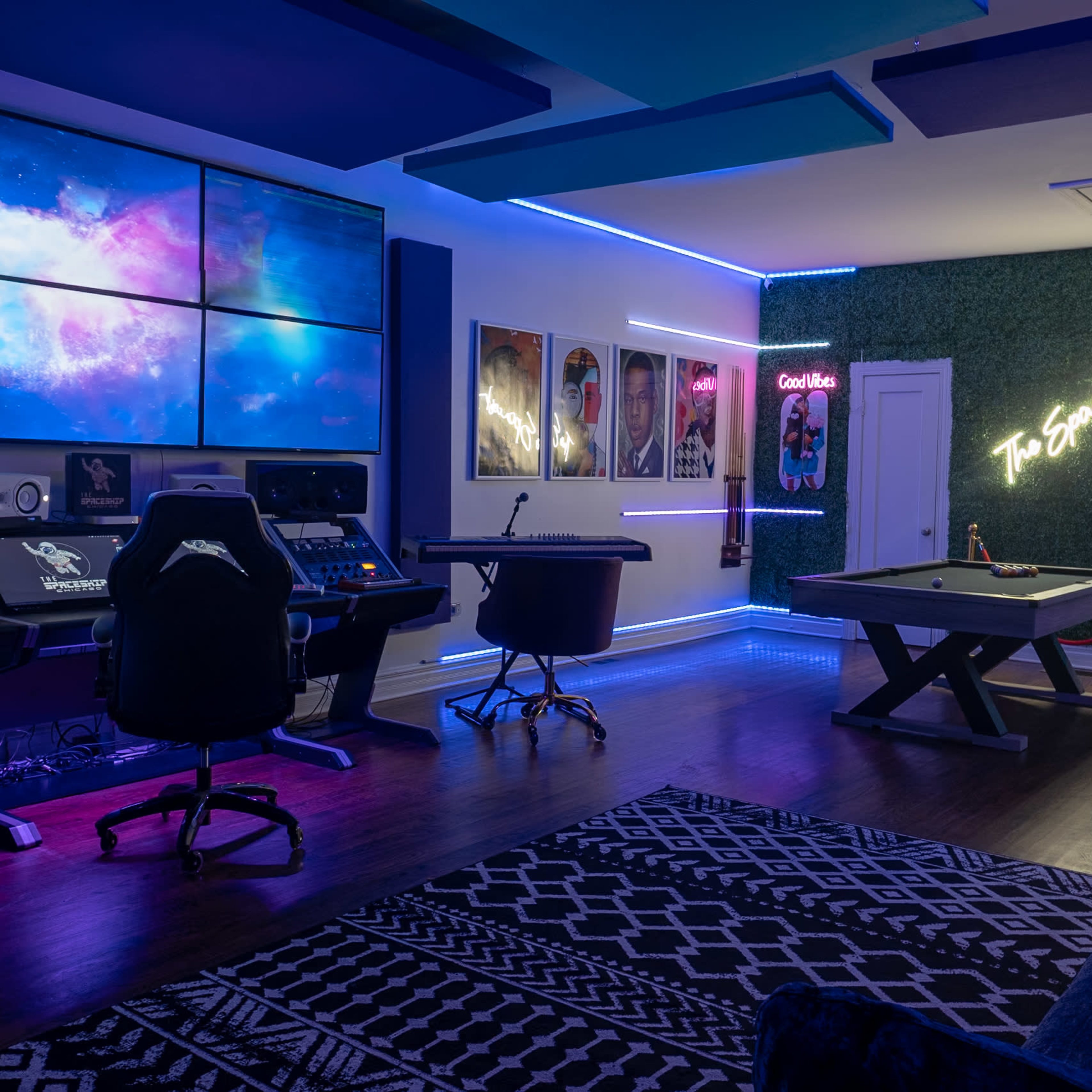 A modern music studio with multiple screens displaying a cosmic scene, surrounded by stylish furniture and vibrant LED lighting.