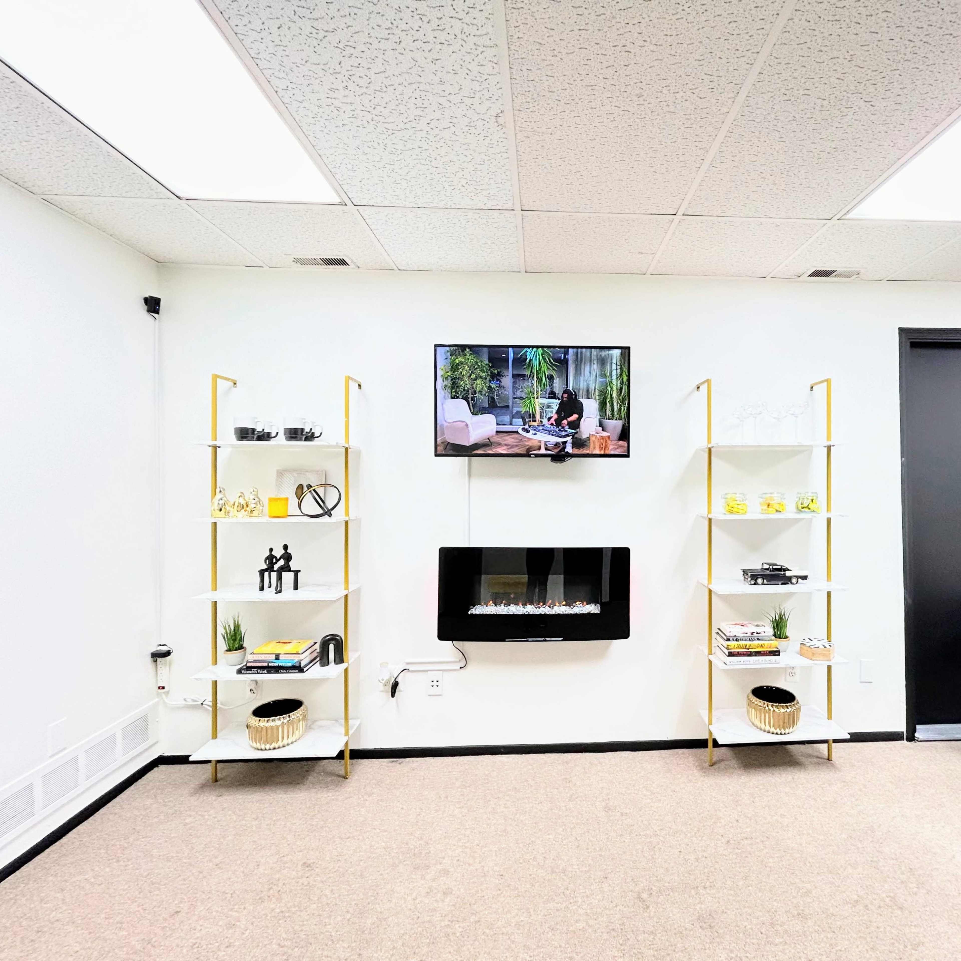 A modern room with two shelving units on either side, a wall-mounted television above an electric fireplace, and a black chair positioned in front.