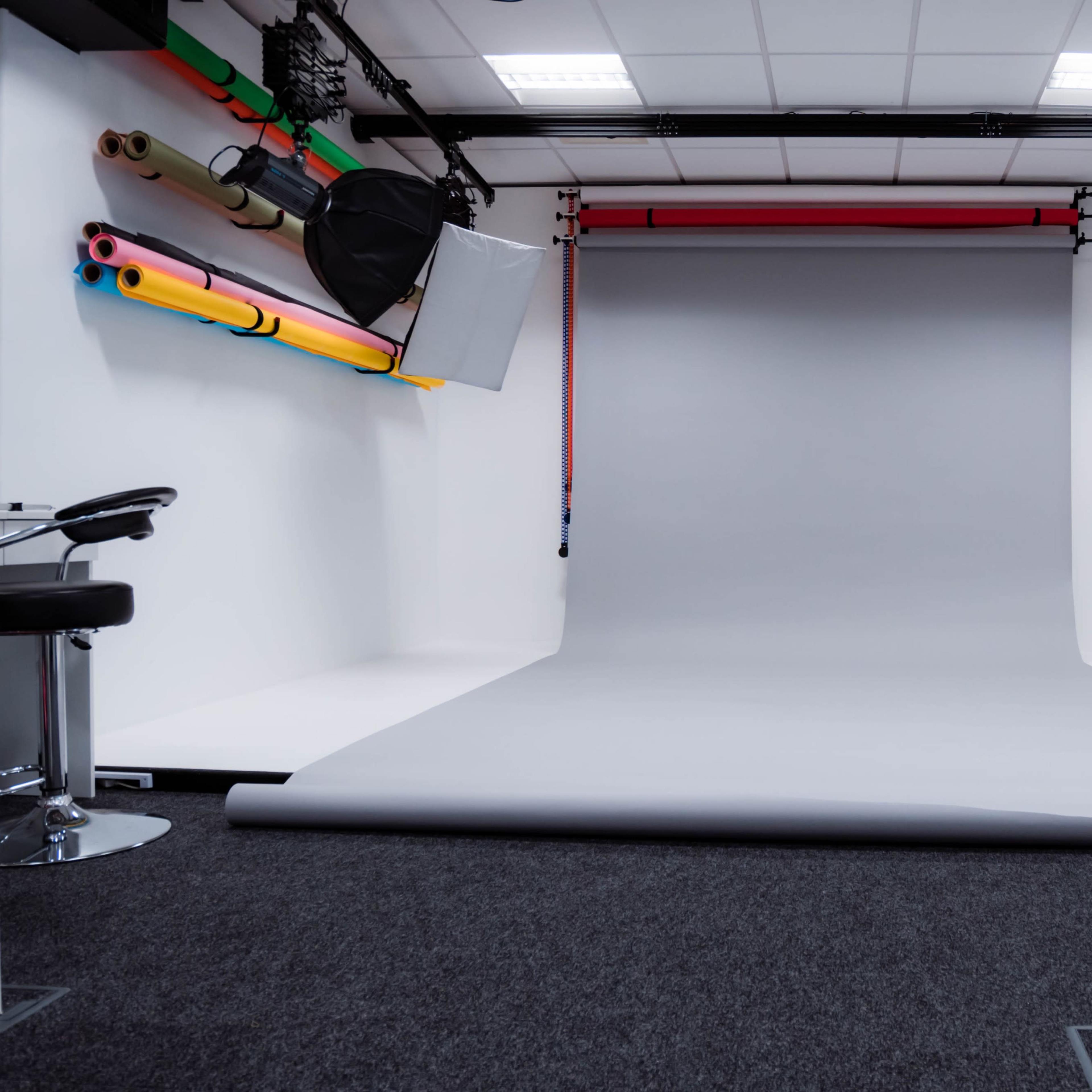 A photography studio with a gray backdrop, two softbox lights, and colorful rolls of backdrop paper mounted on the wall.