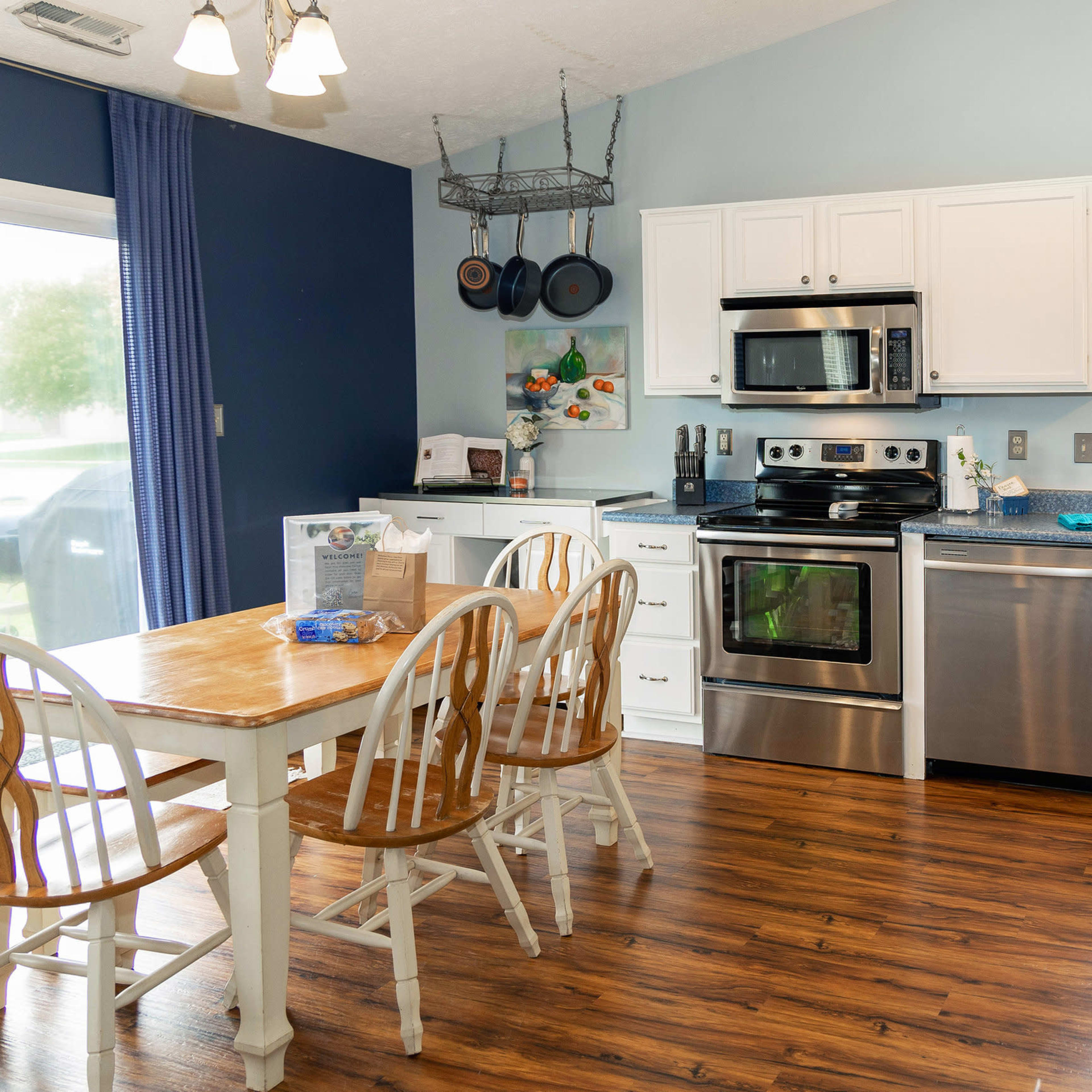 A kitchen with white cabinets, stainless steel appliances, a wooden dining table with white chairs, and blue walls.