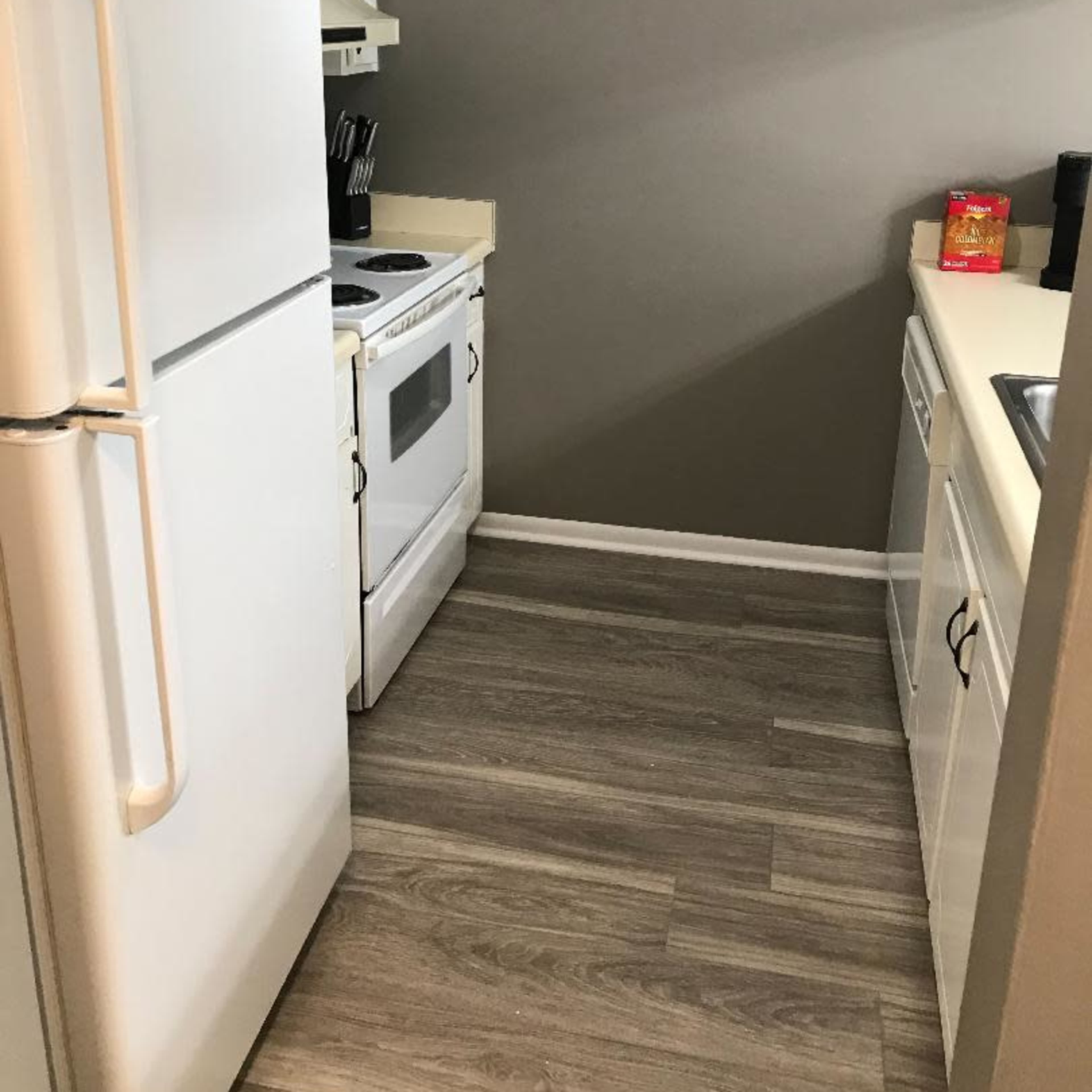 A compact kitchen with a refrigerator, stove, and sink, featuring light-colored cabinets and laminate flooring.