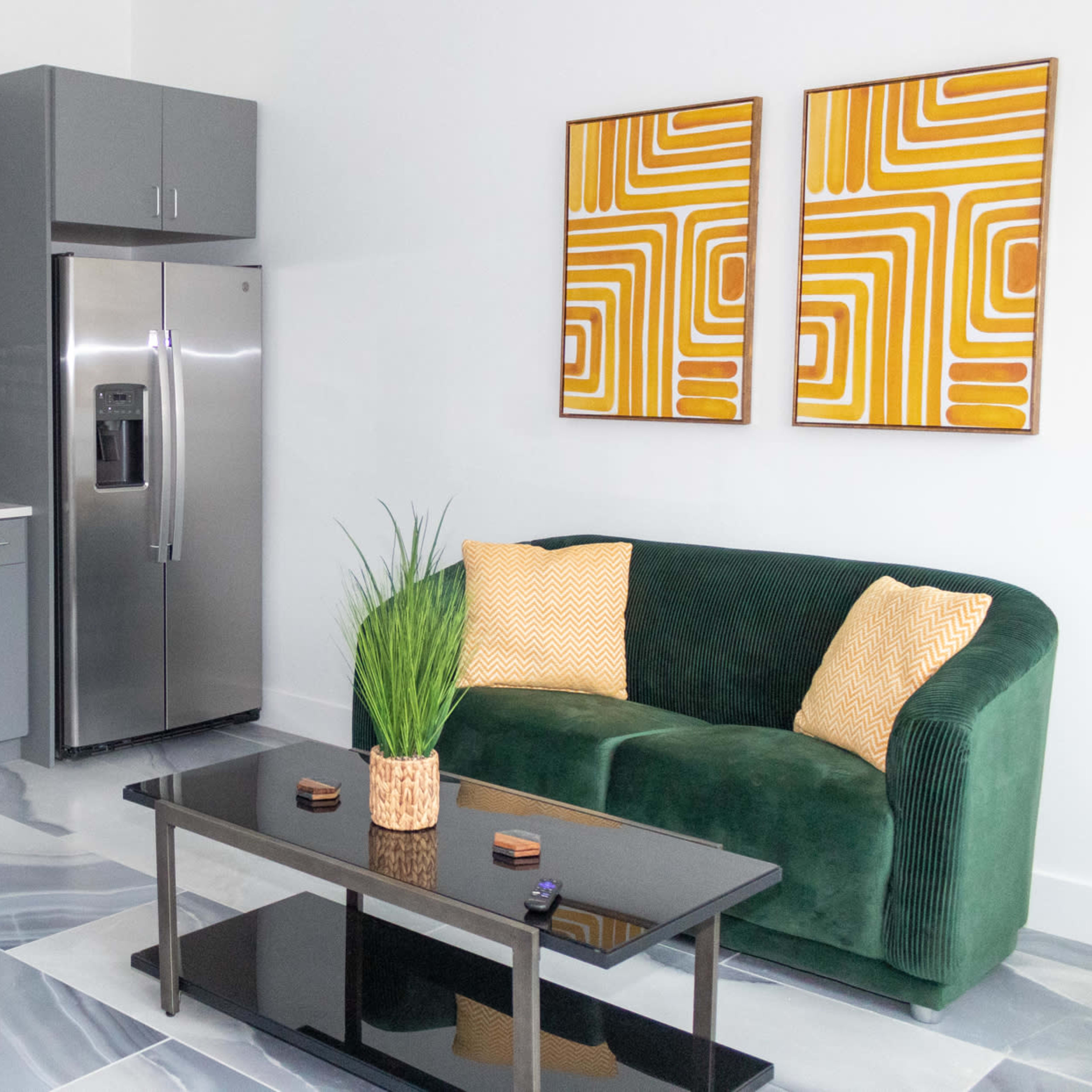 A modern kitchen and living area that features gray cabinets, stainless steel appliances, a green sofa, and abstract wall art.