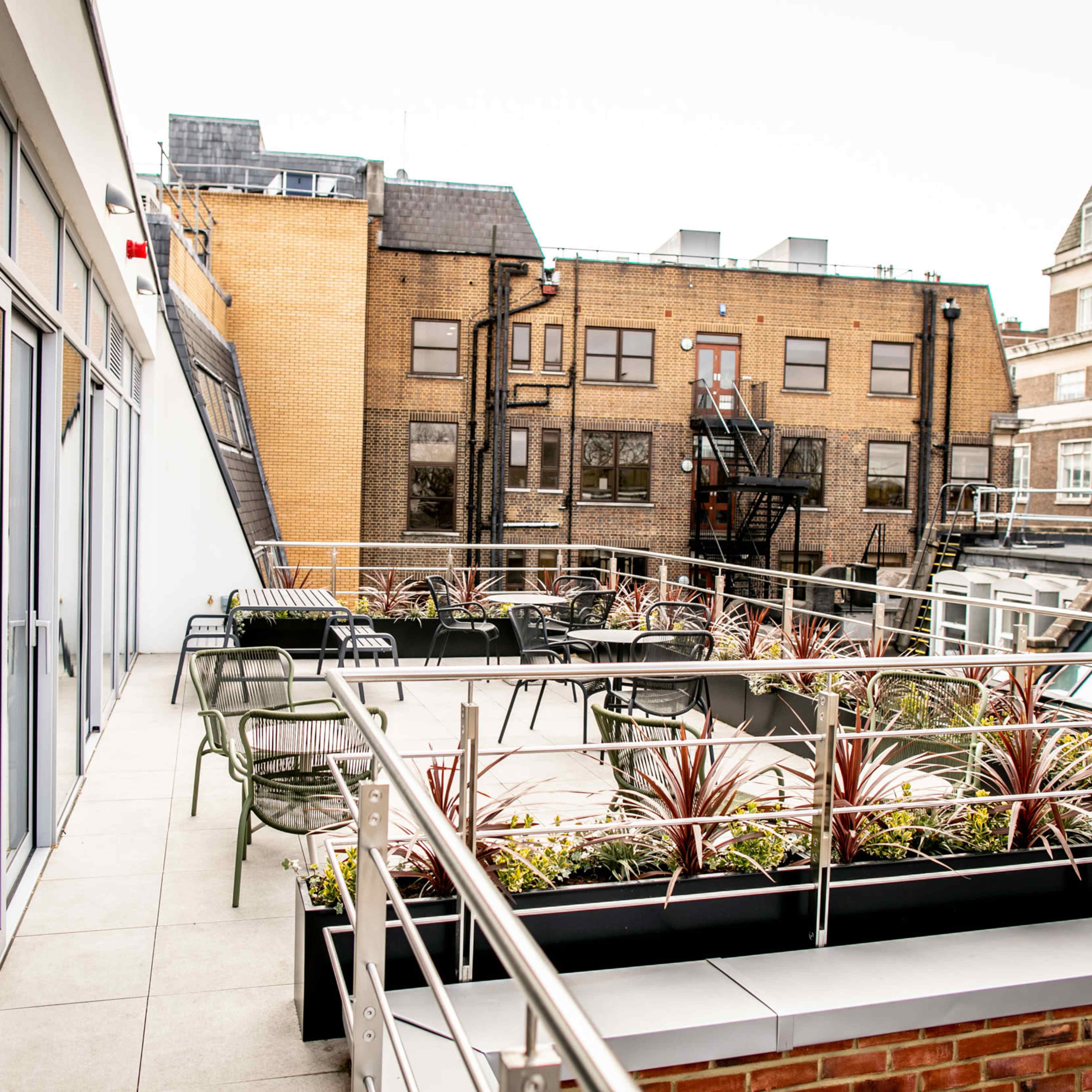 A rooftop terrace with seating and planters surrounded by brick and glass buildings.
