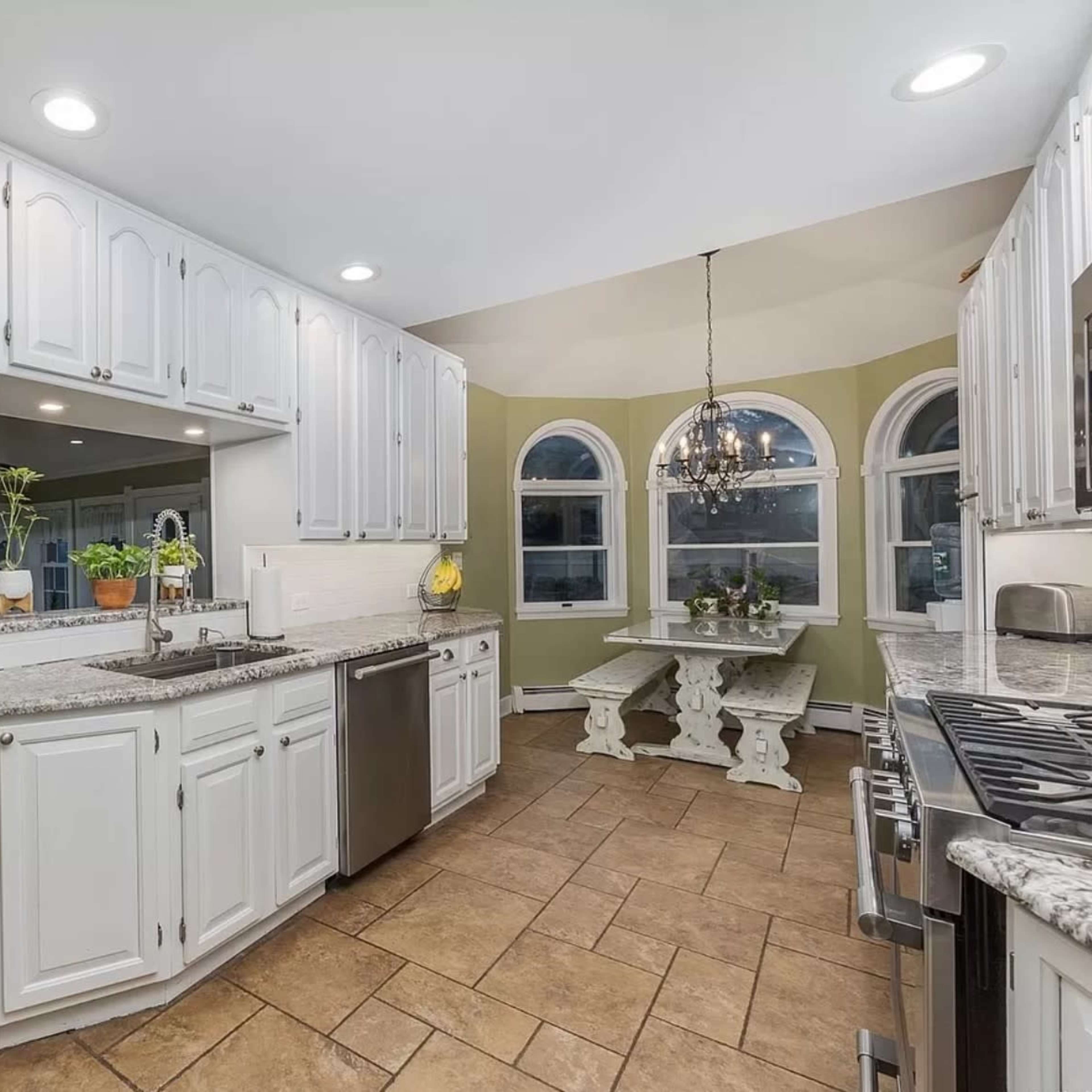 A kitchen with white cabinets, granite countertops, and a dining area featuring a round table and chairs beneath a chandelier.