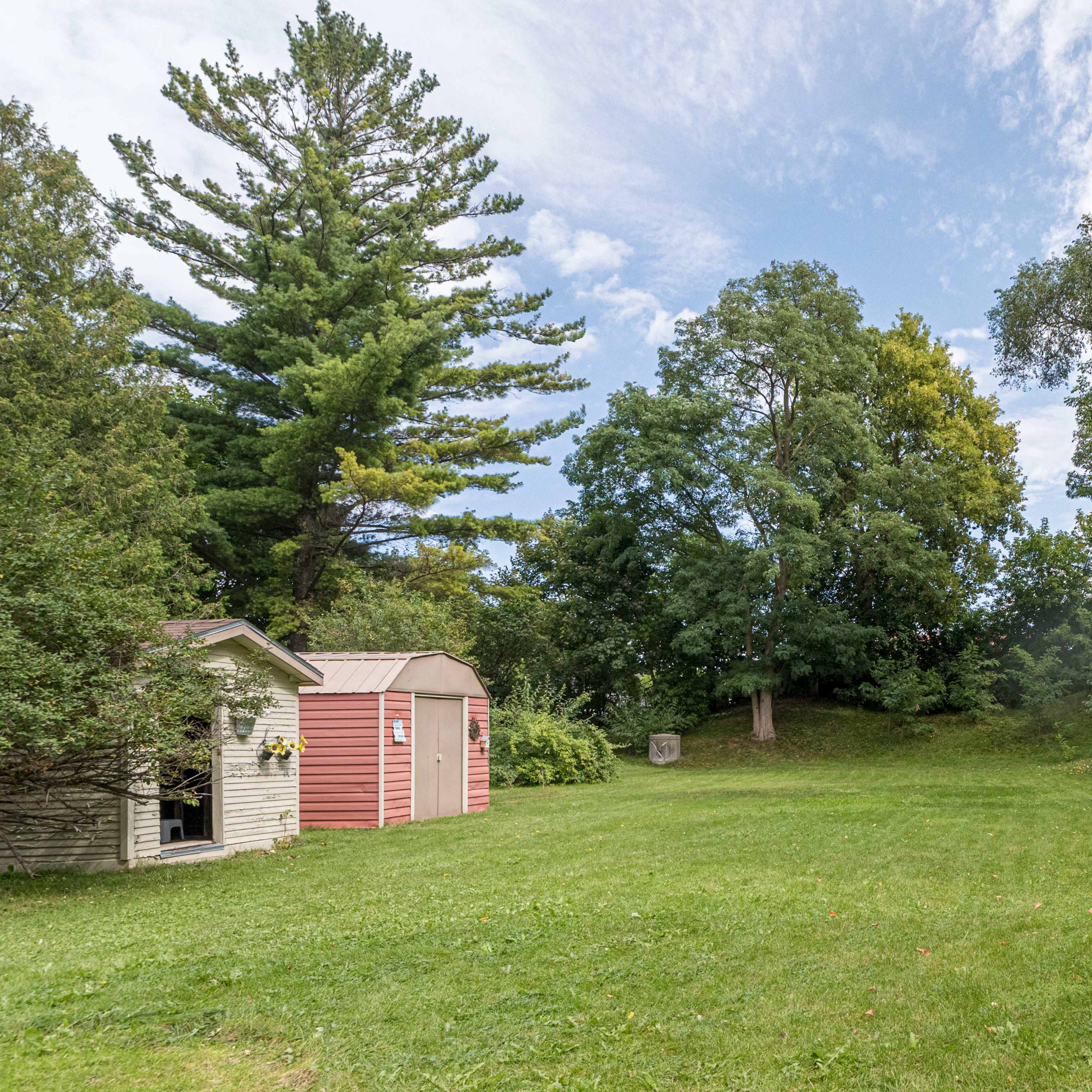 A small pink shed stands on a grassy area surrounded by trees under a partly cloudy sky.
