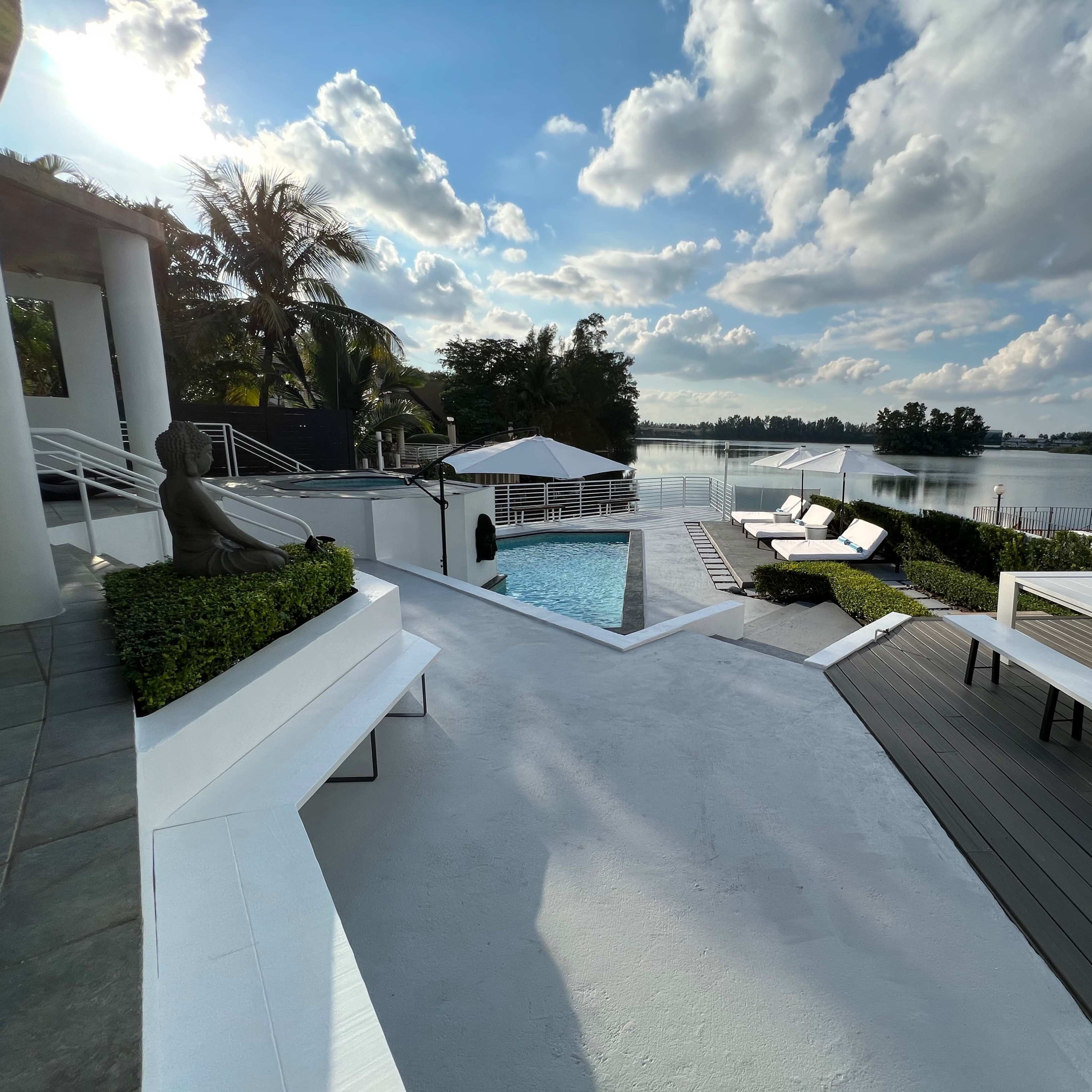 A modern outdoor space featuring a pool, lounge chairs, and a waterfront view with scattered clouds in the sky.