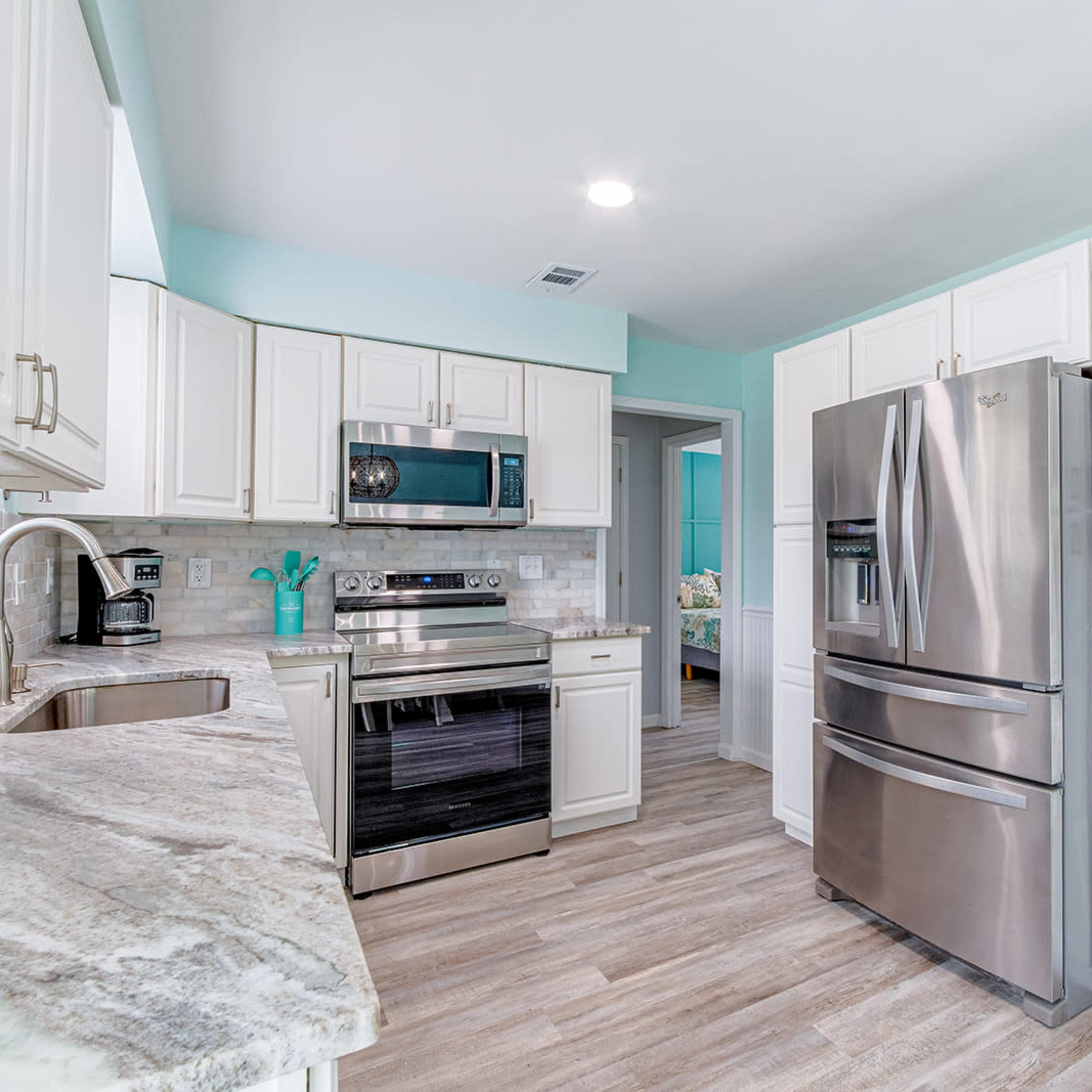 A modern kitchen features stainless steel appliances, light cabinetry, and a marble countertop.