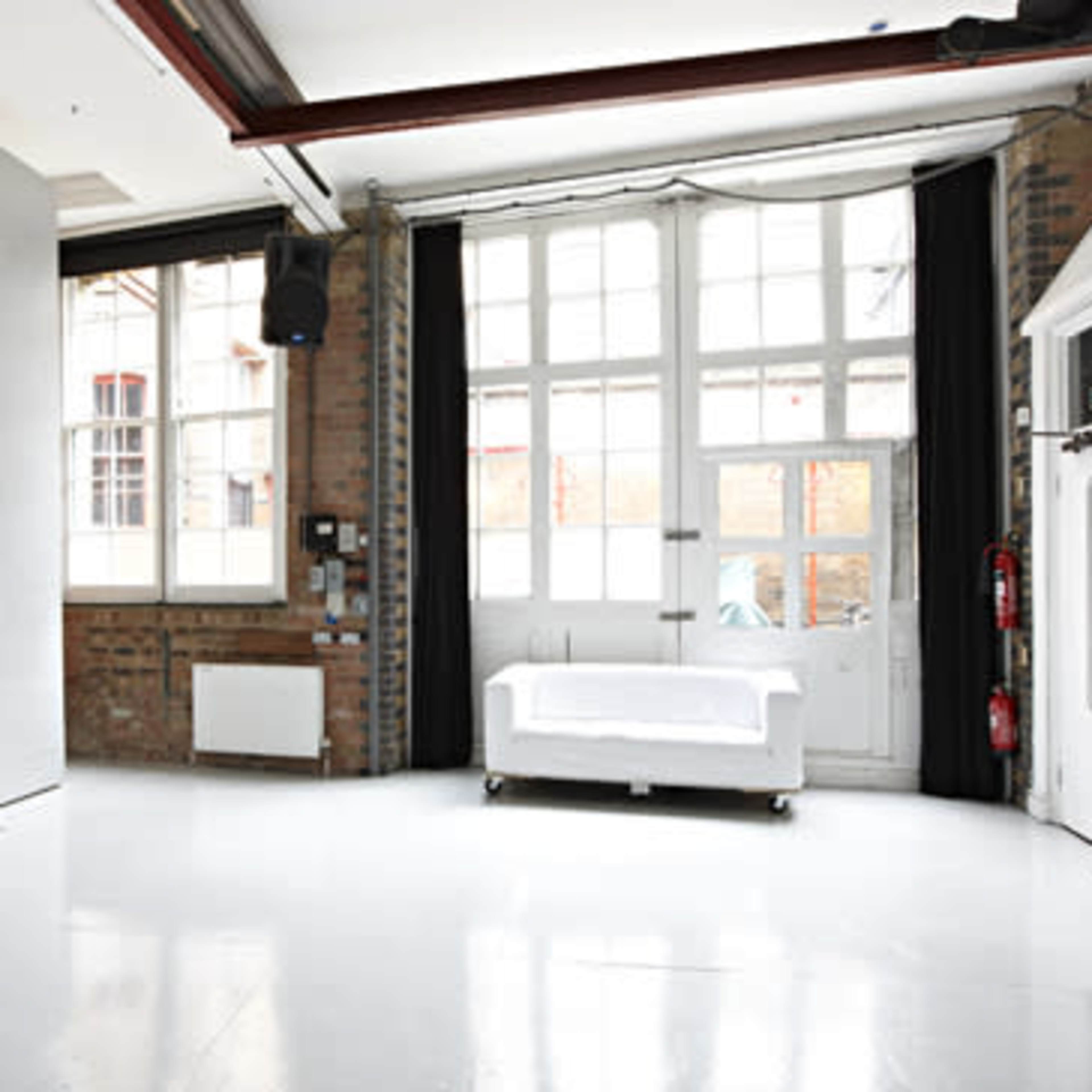 A spacious, empty room with large windows, white walls, a white sofa in the center, and brick accents.
