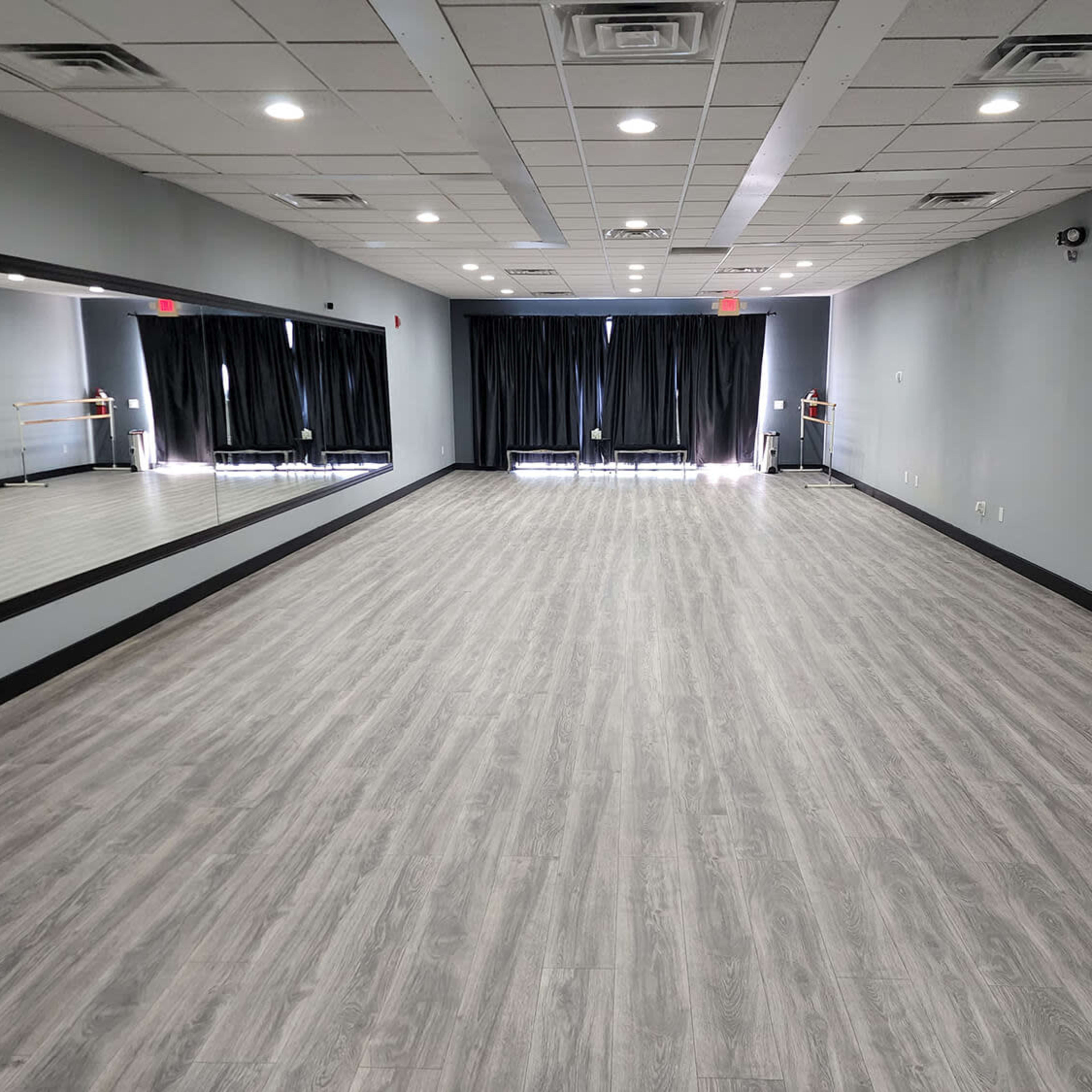 A spacious dance studio with gray walls, a large mirror on one side, and black curtains covering the windows.