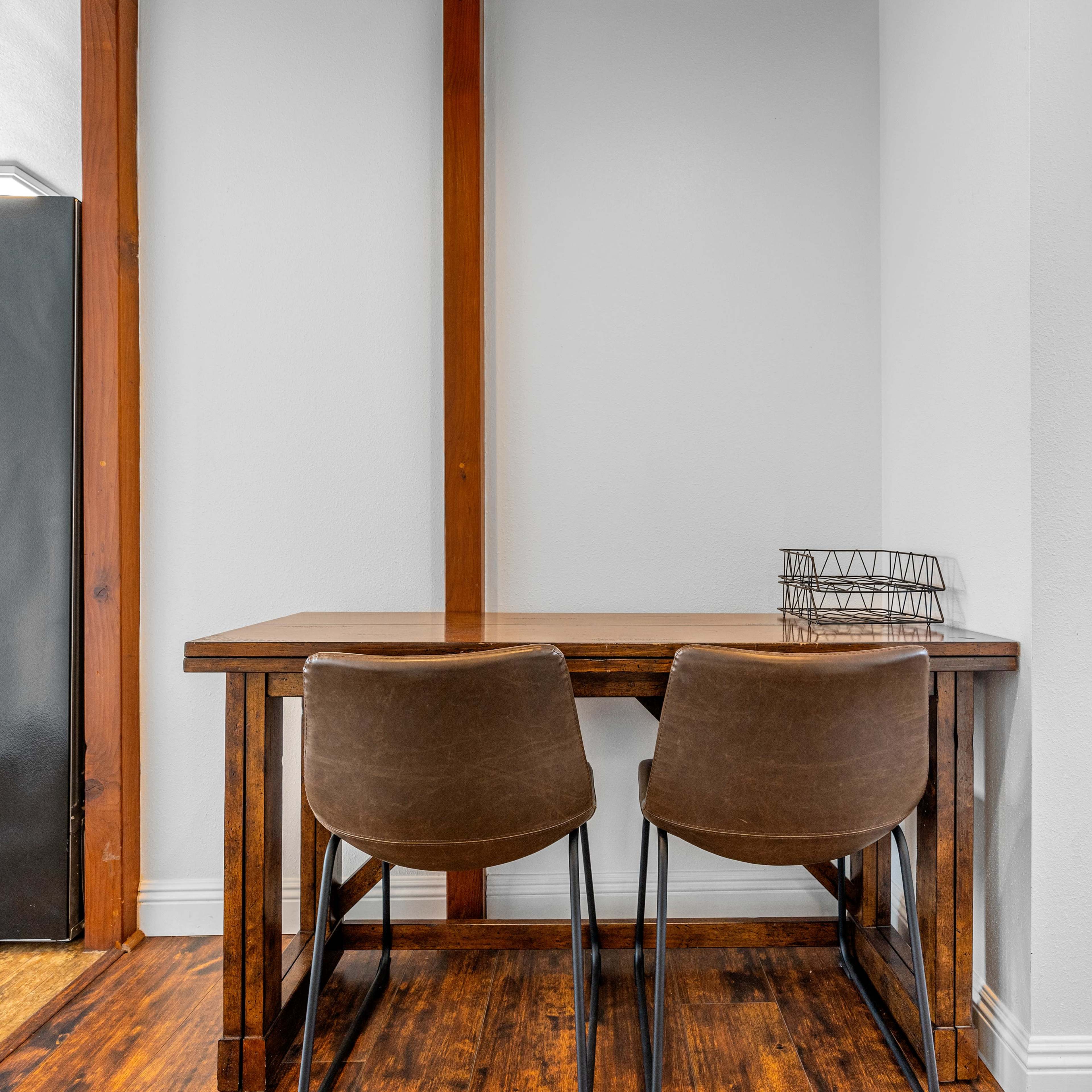 A small wooden table with two brown chairs is positioned against a wall in a brightly lit room.
