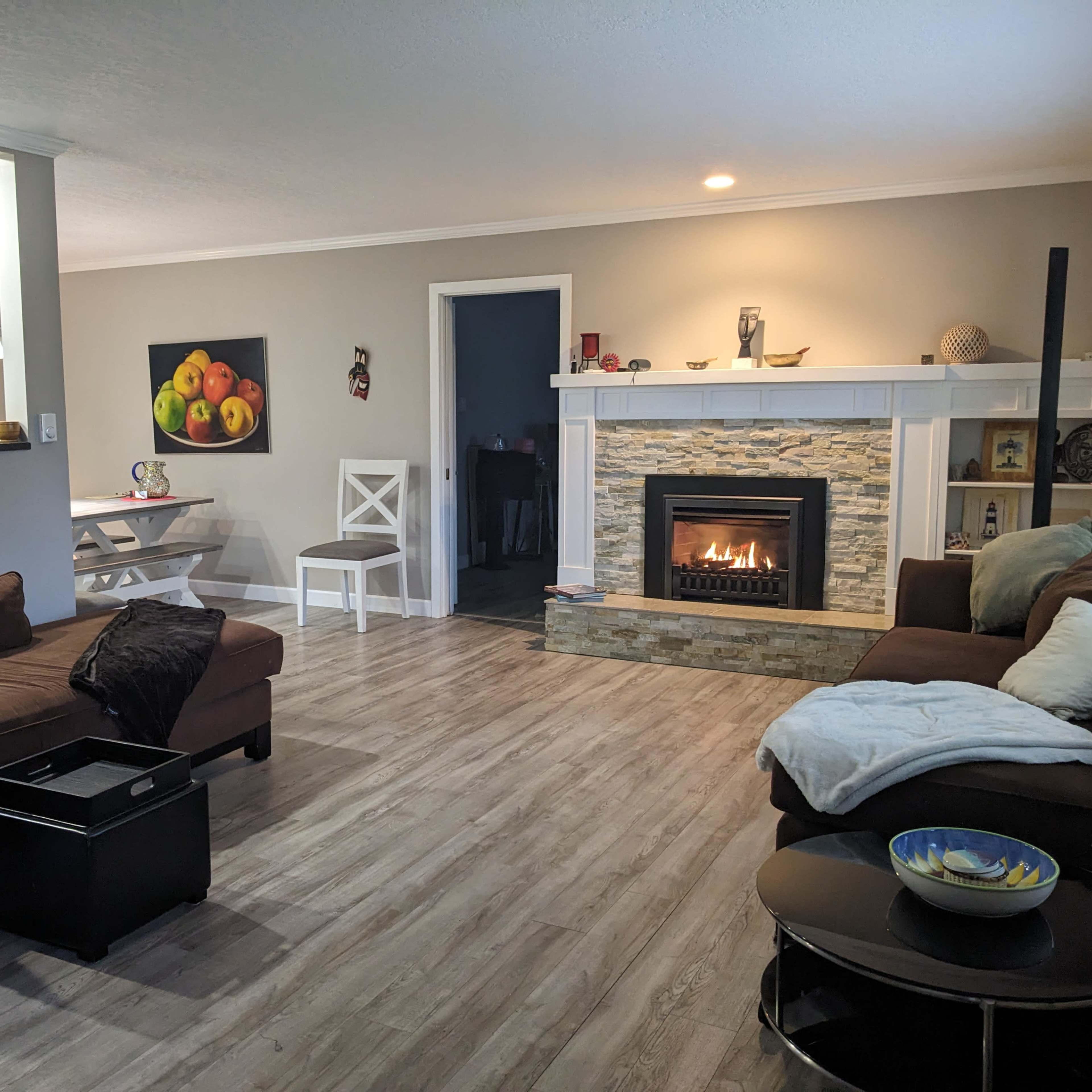 A living room with a stone fireplace, a brown sectional sofa, a white dining table, and a decorative bowl on a coffee table.