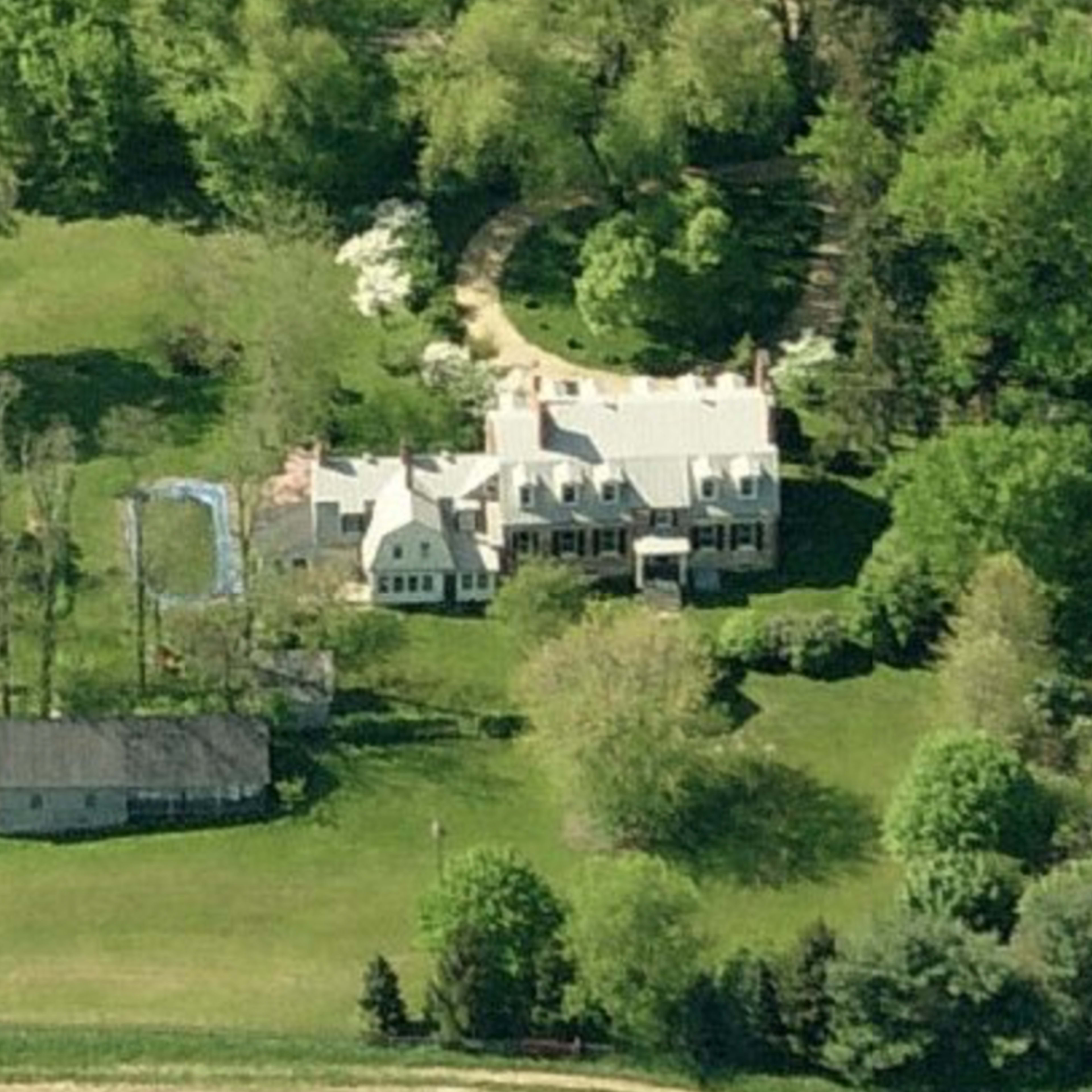 An aerial view shows a large house surrounded by trees, a swimming pool, and a tennis court nearby.