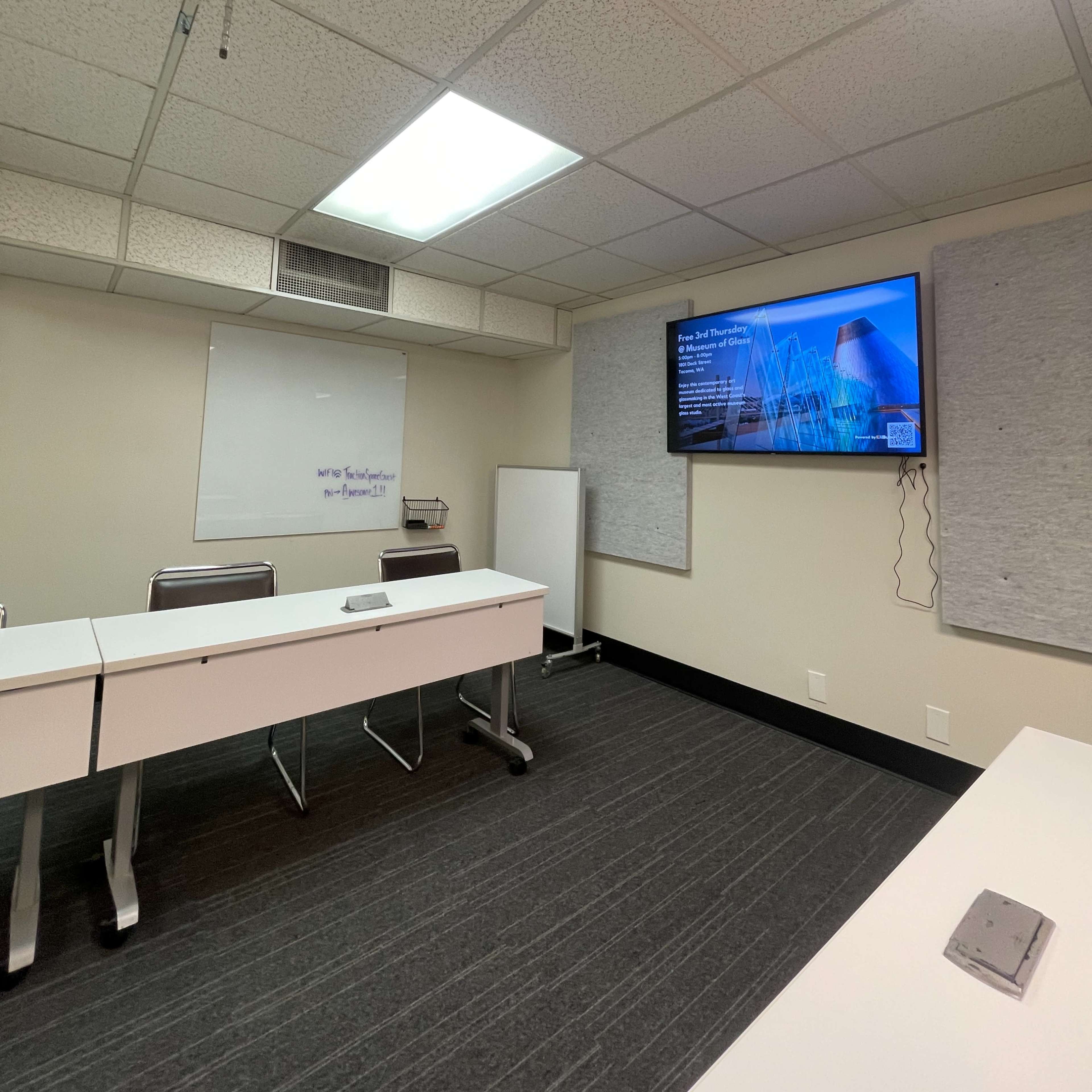 A conference room with a large screen displaying a presentation, whiteboards, and a long table with chairs.