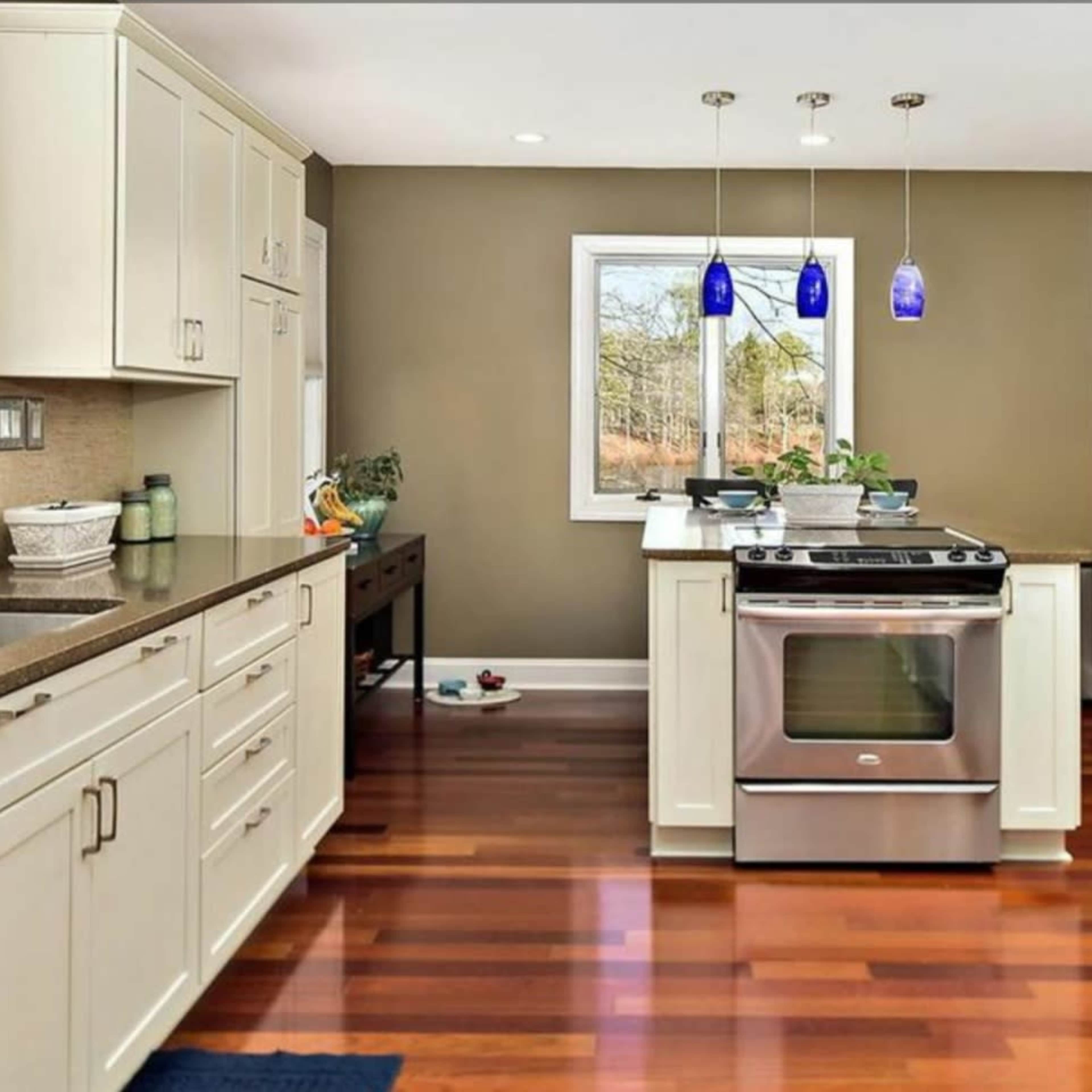 A modern kitchen with white cabinetry, stainless steel appliances, and dark wood flooring.