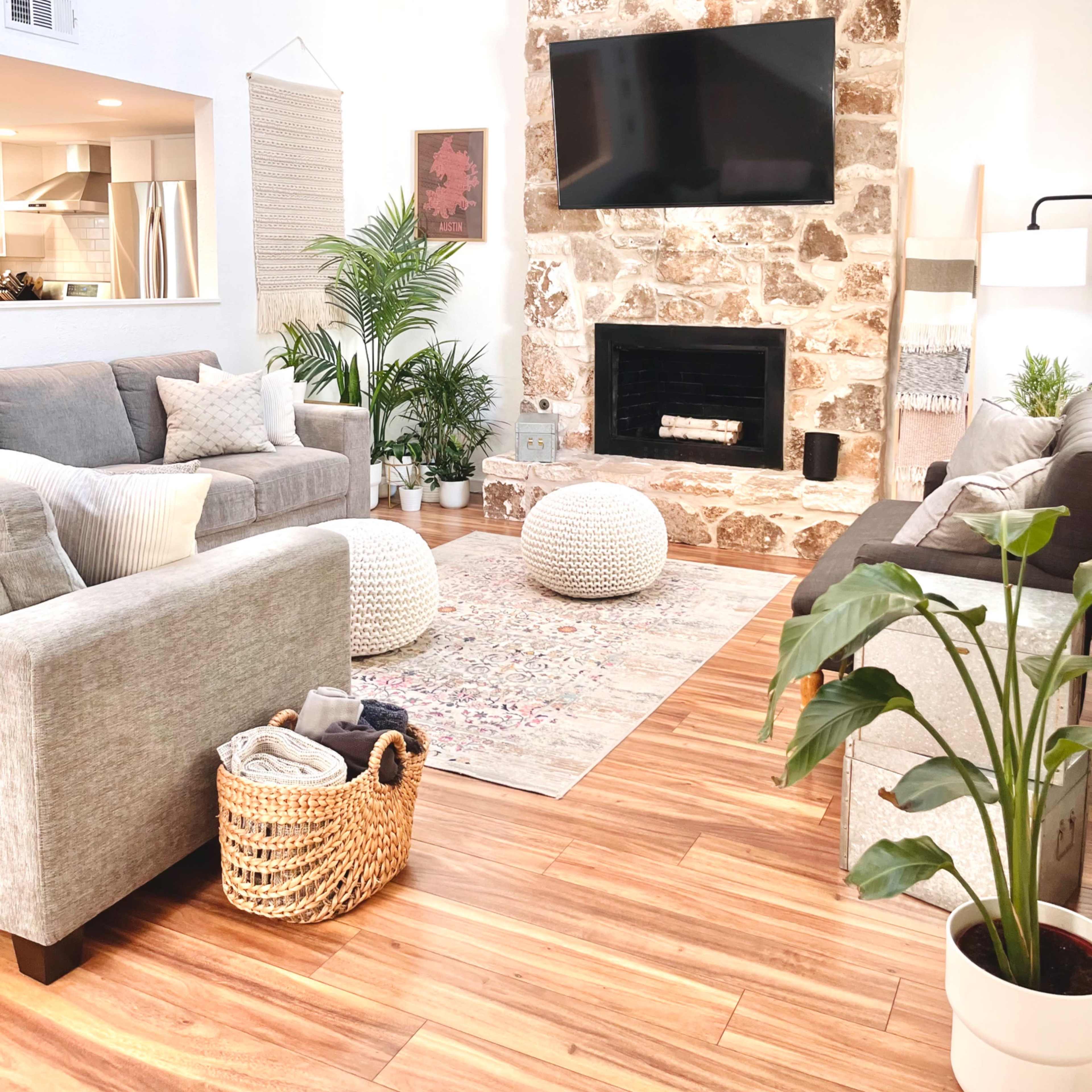 The living room features a stone fireplace, a mounted television, various seating arrangements, and natural light streaming in.