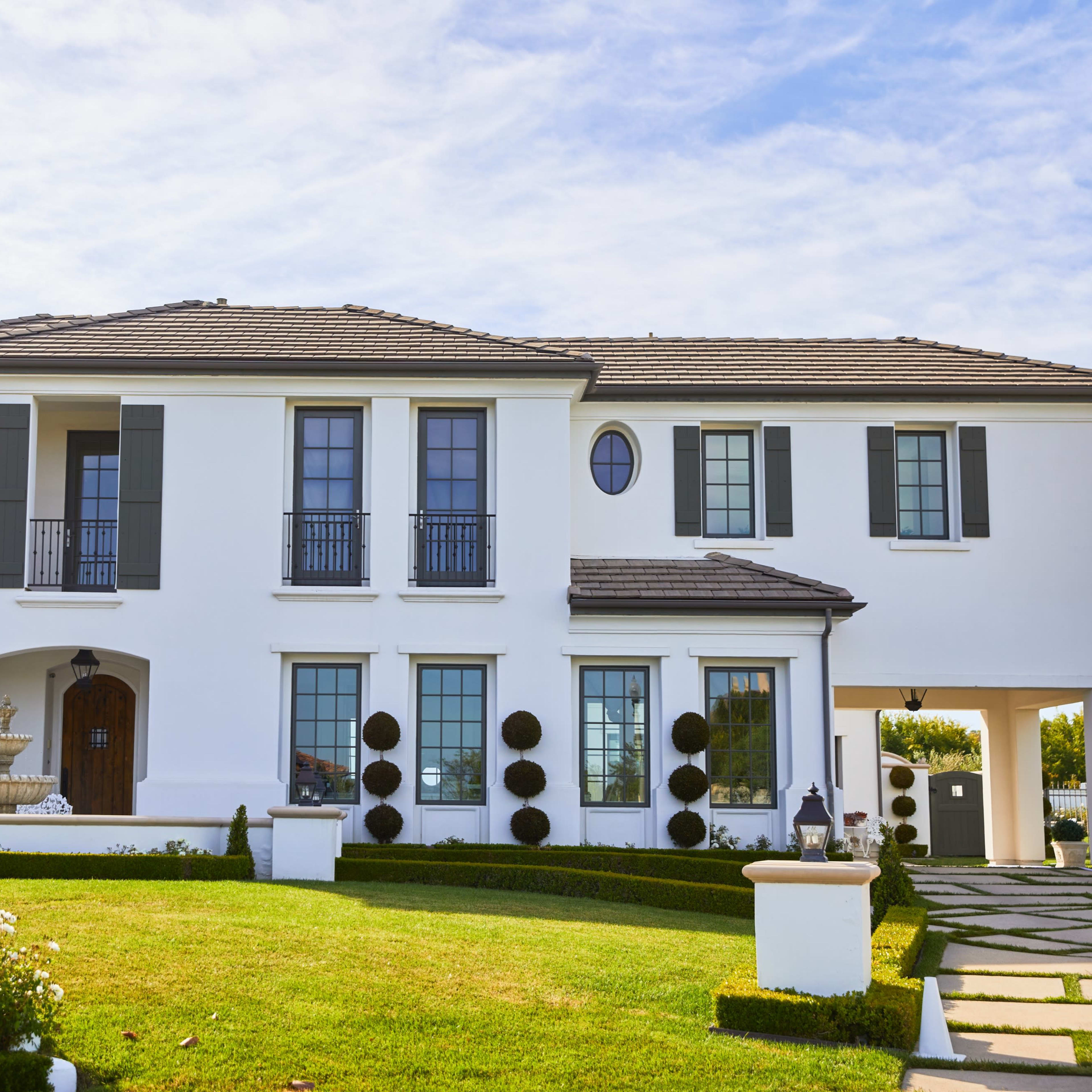 A two-story white house with a tiled roof, surrounded by neatly trimmed hedges and a well-maintained lawn.
