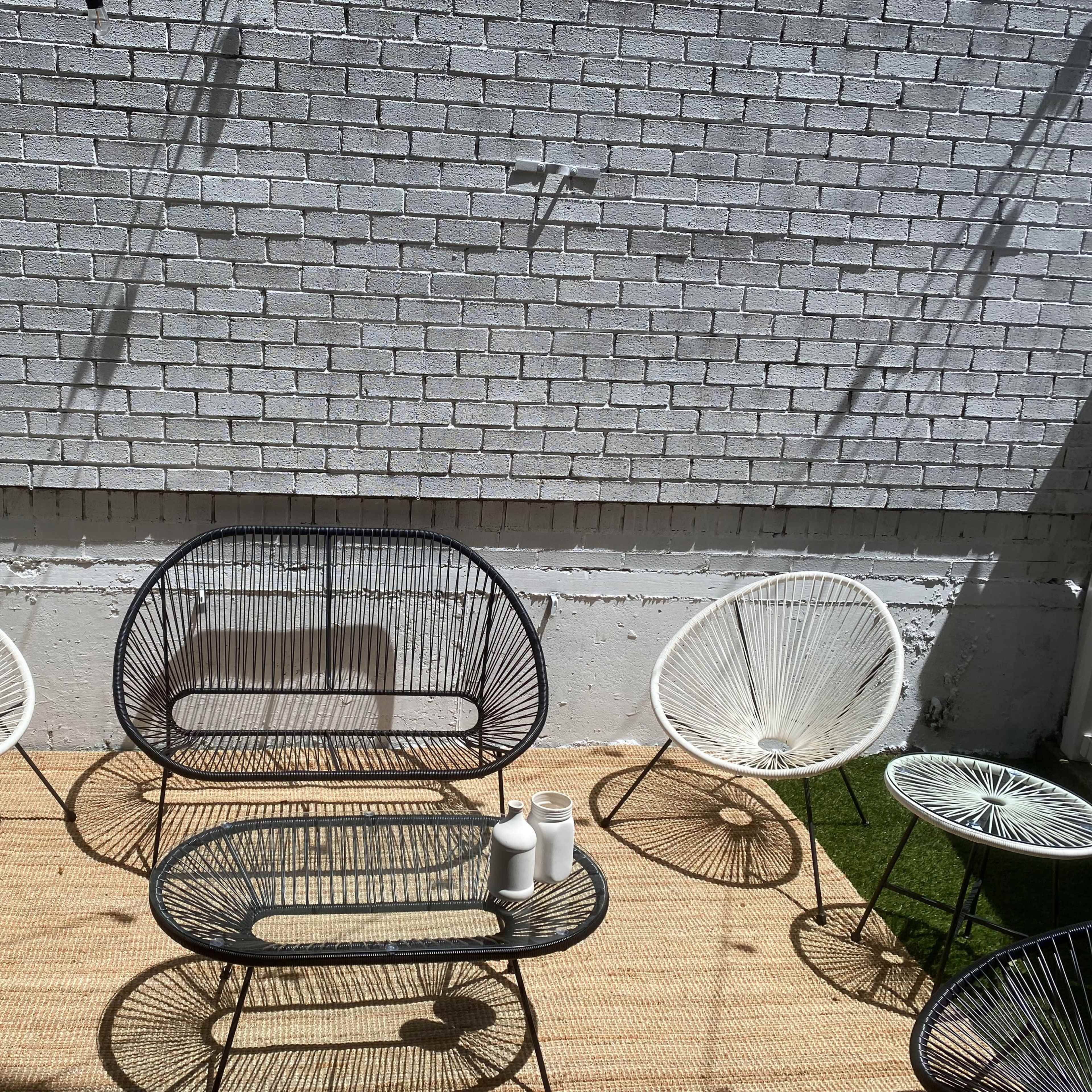 A patio area with minimalist metal chairs and a central coffee table, all positioned on a carpet of grass under a bright sun.