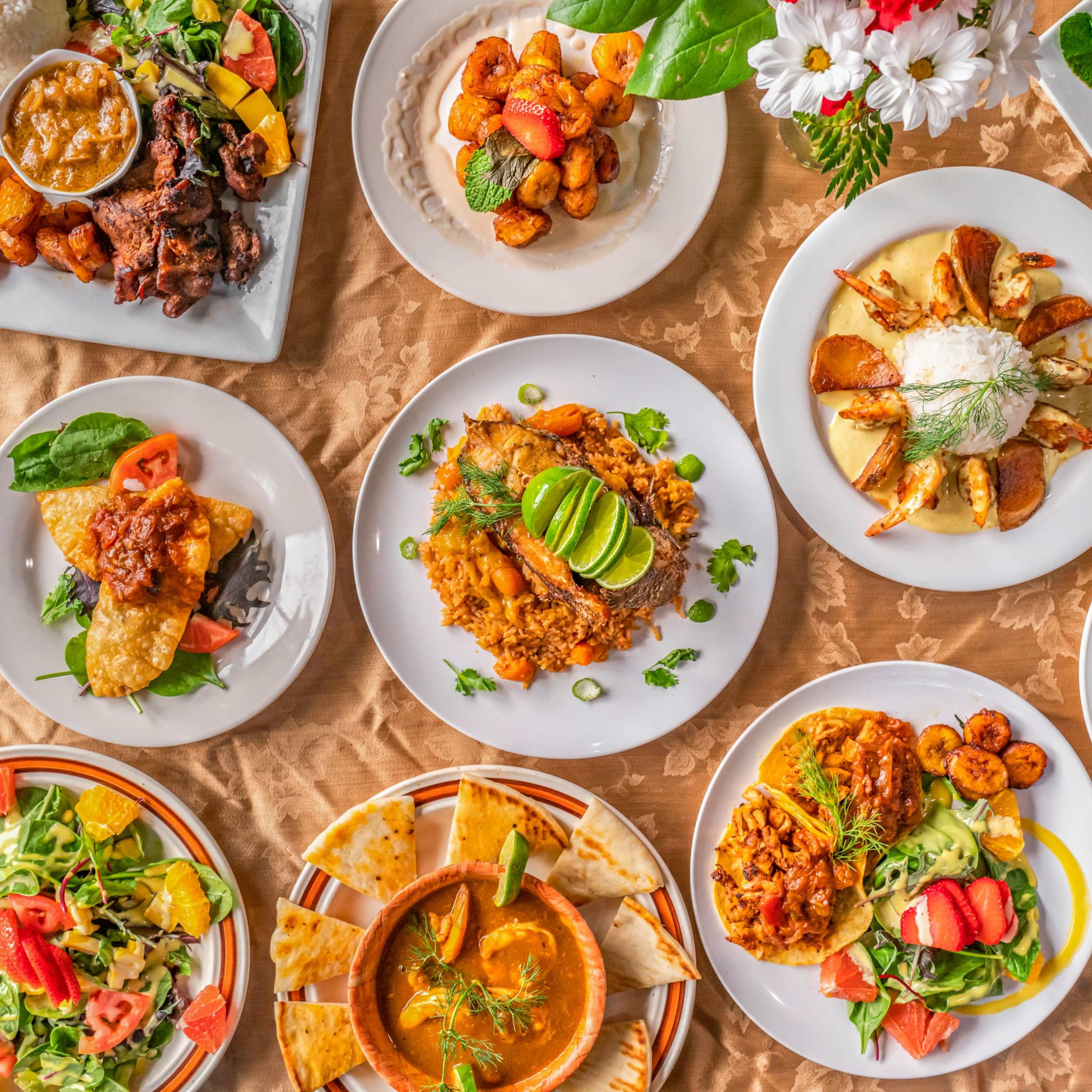 A vibrant array of various dishes including rice, seafood, salads, and fried plantains arranged on a tablecloth.