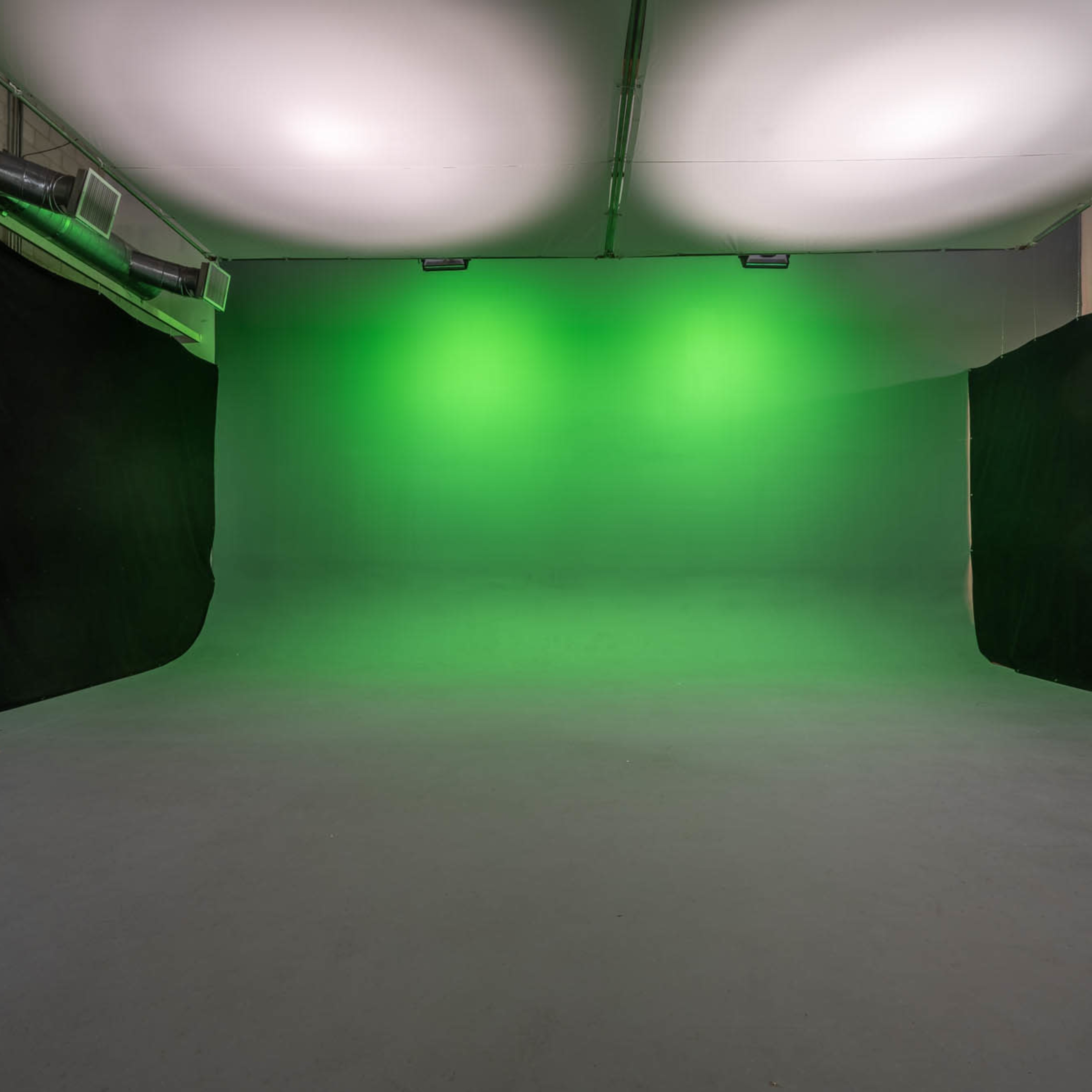 An empty studio space with a green backdrop and black drapes on either side.