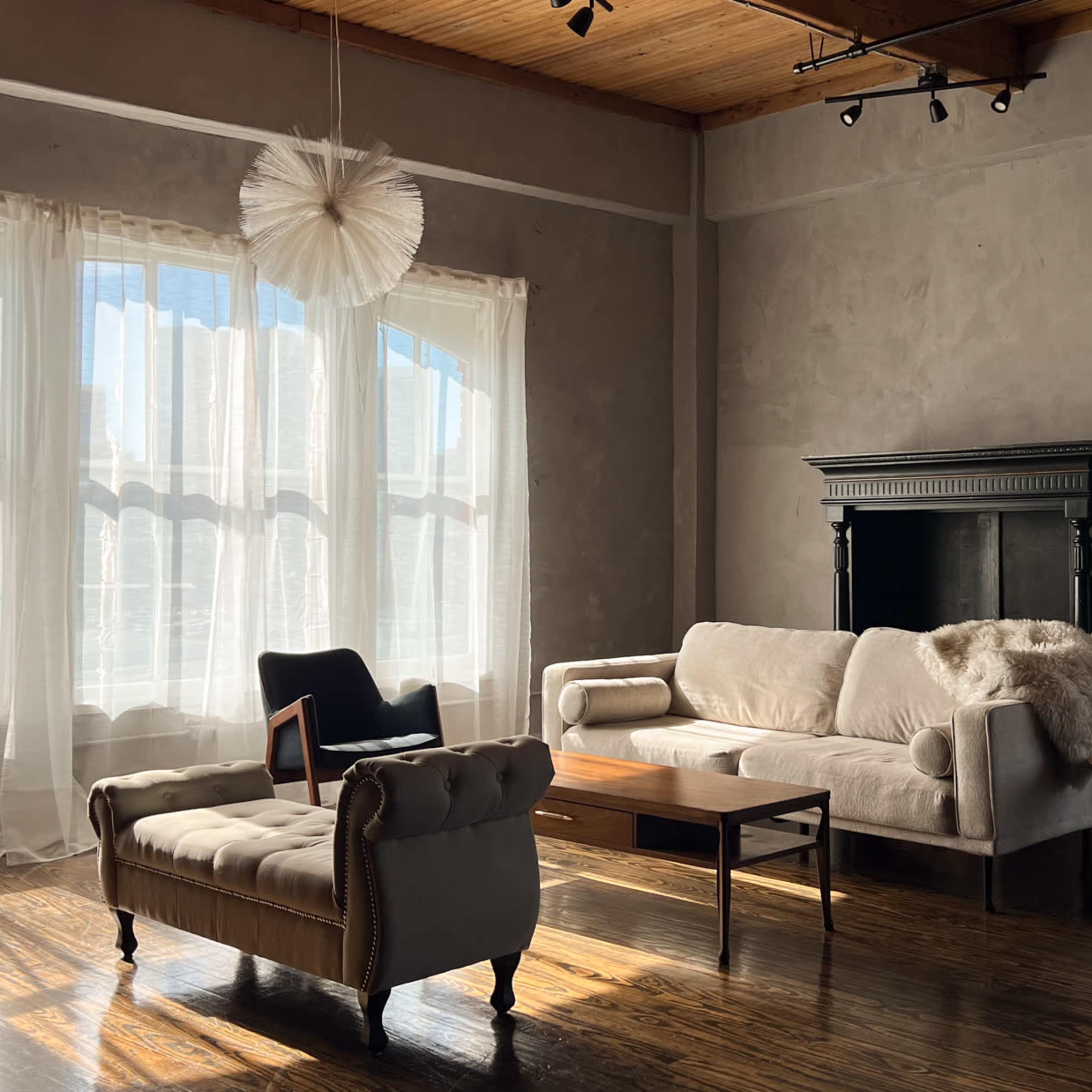 A modern living room features a light-colored sofa, a wooden coffee table, and a fireplace, with large windows allowing natural light to fill the space.