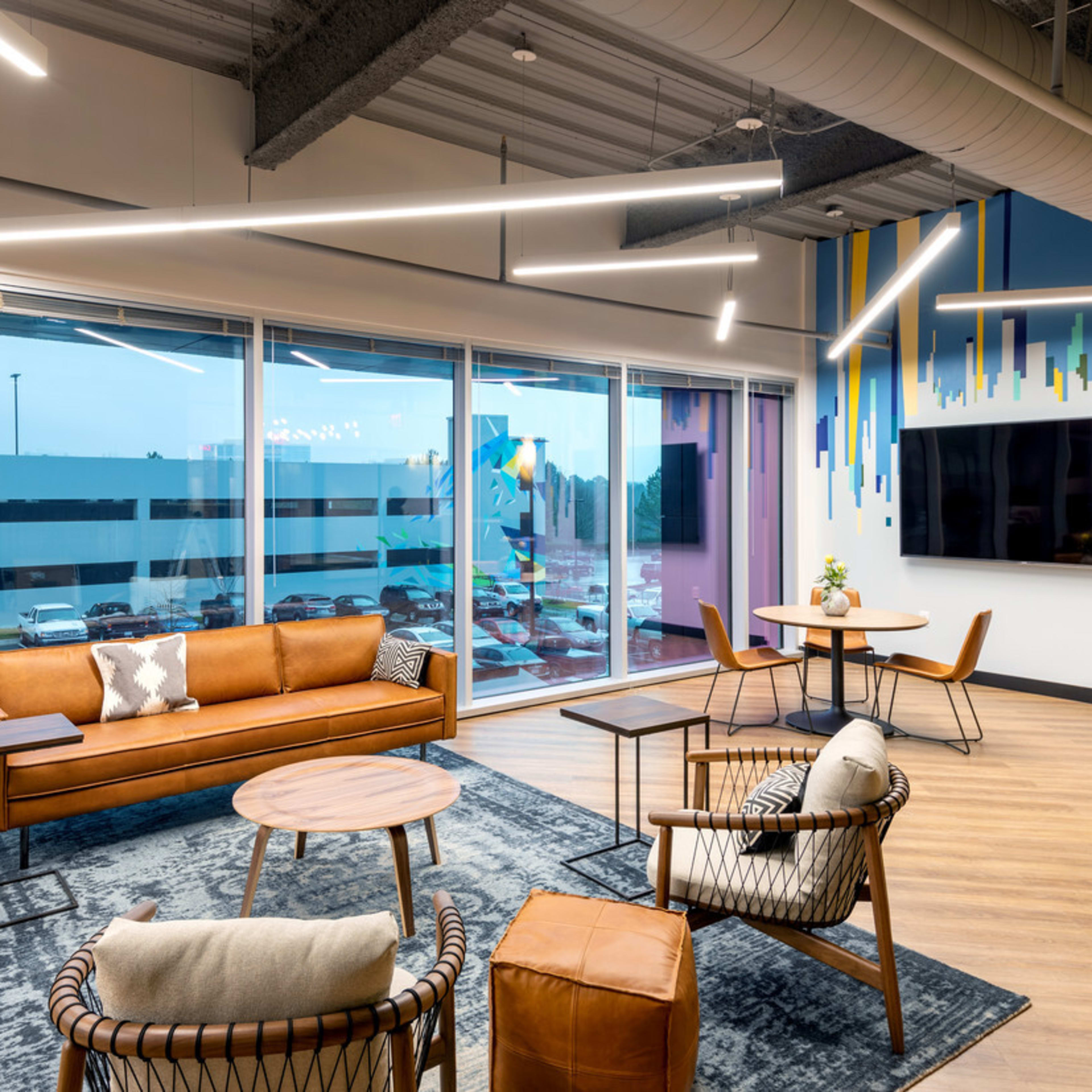 A modern lounge area featuring a brown leather couch, stylish armchairs, a coffee table, and large windows with a view of an outdoor space.