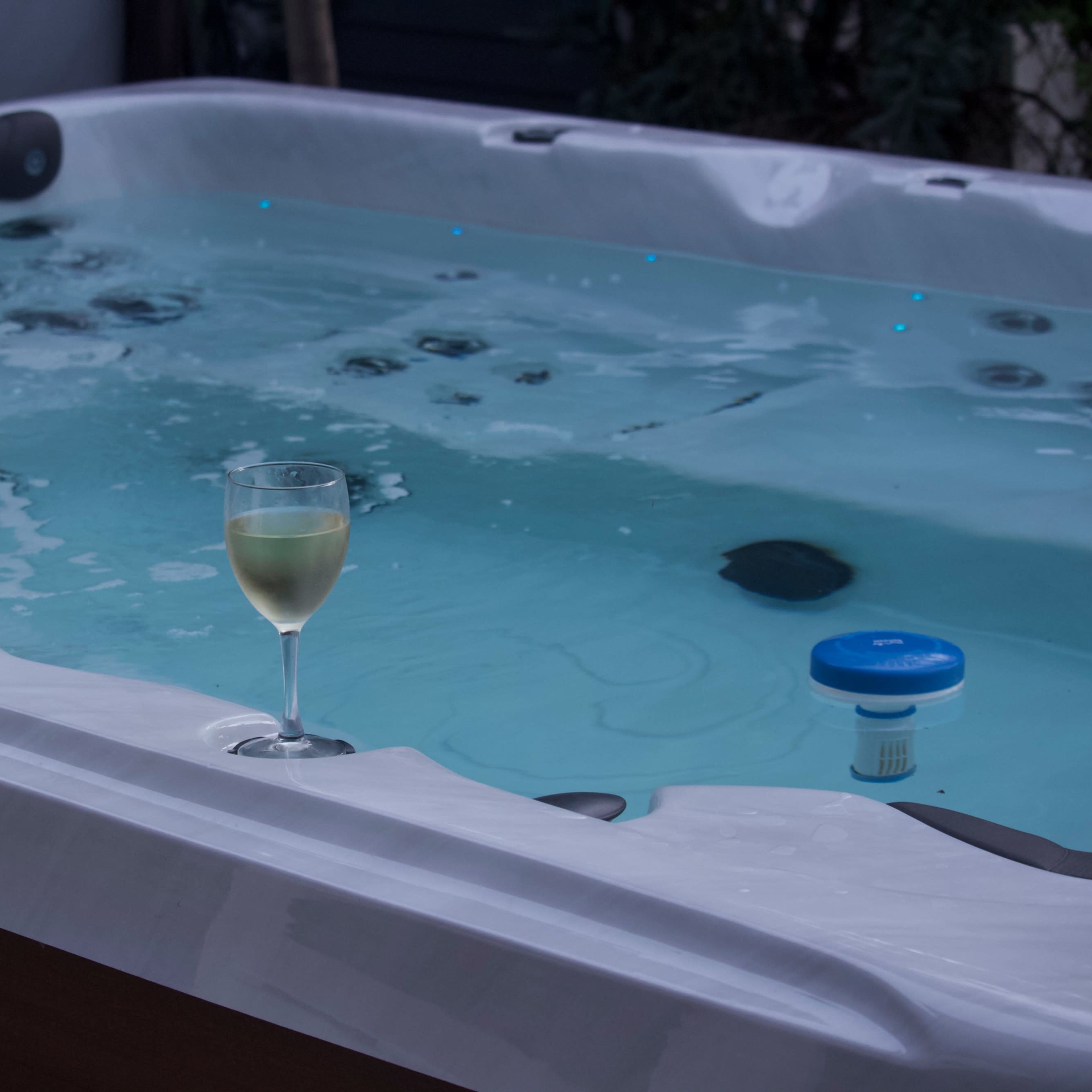 A wine glass rests on the edge of a bubbling hot tub filled with water.