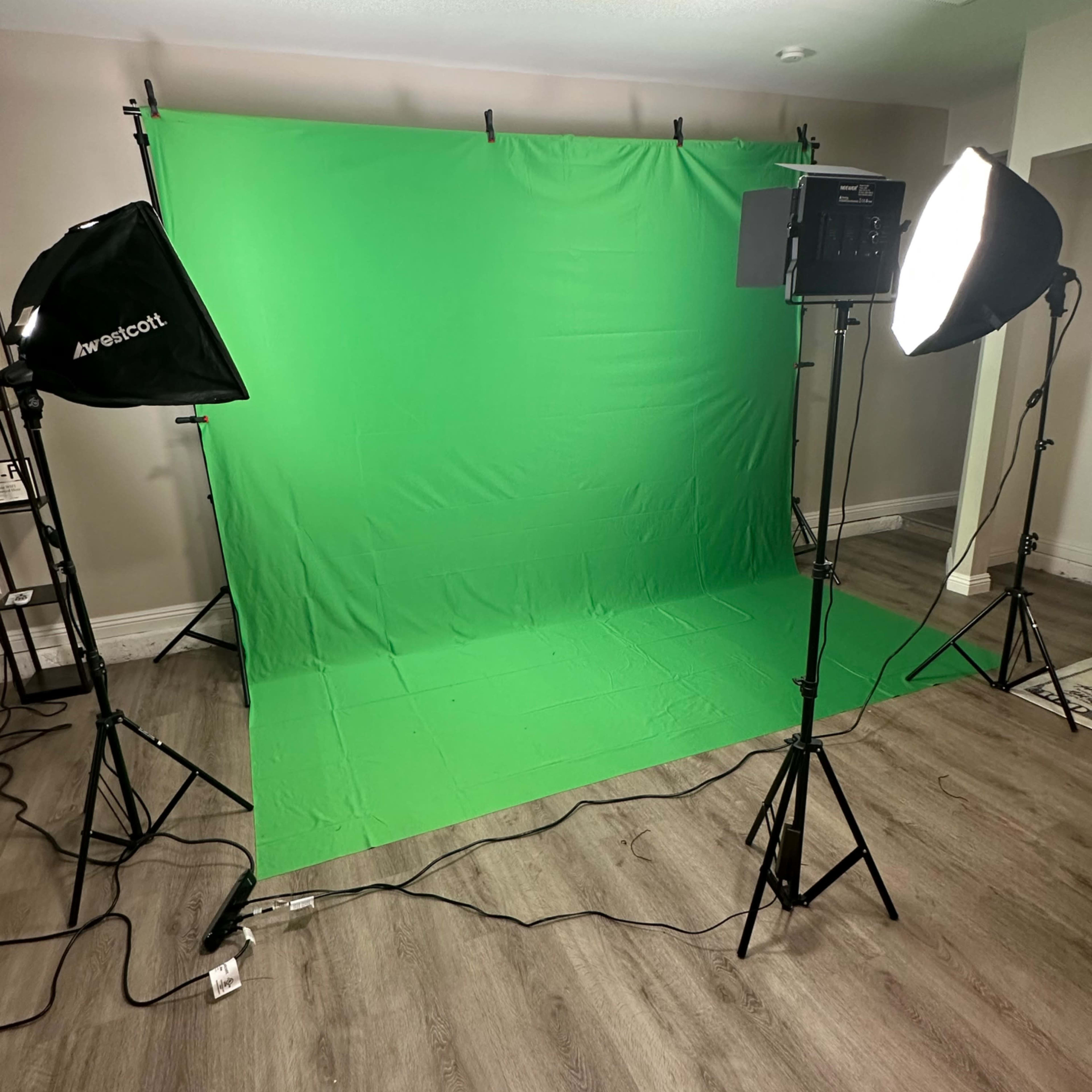 A studio setup with a green screen backdrop, two softbox lights, and a wooden floor.
