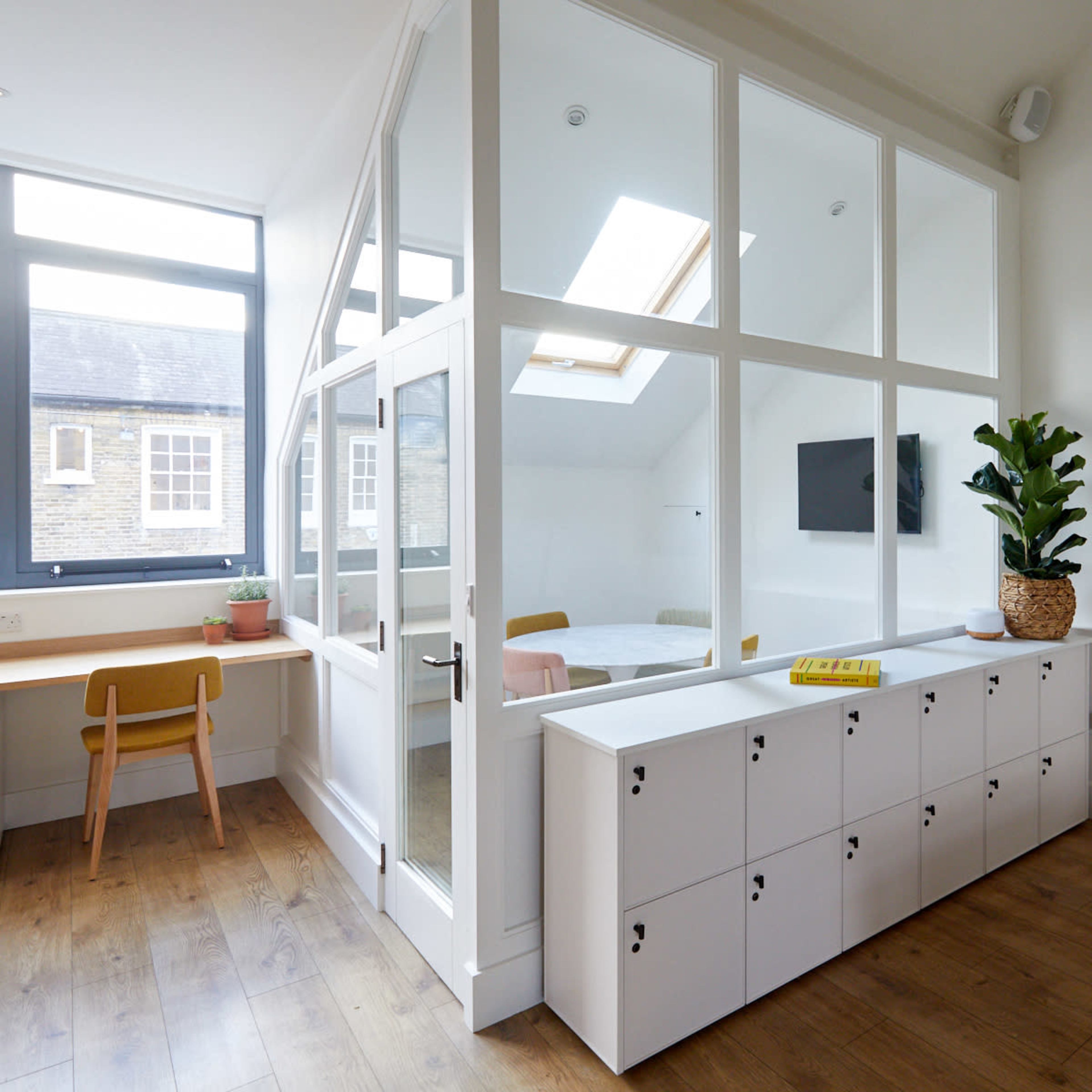 A modern interior with a glass-enclosed room, wooden flooring, and a white storage unit featuring multiple compartments.