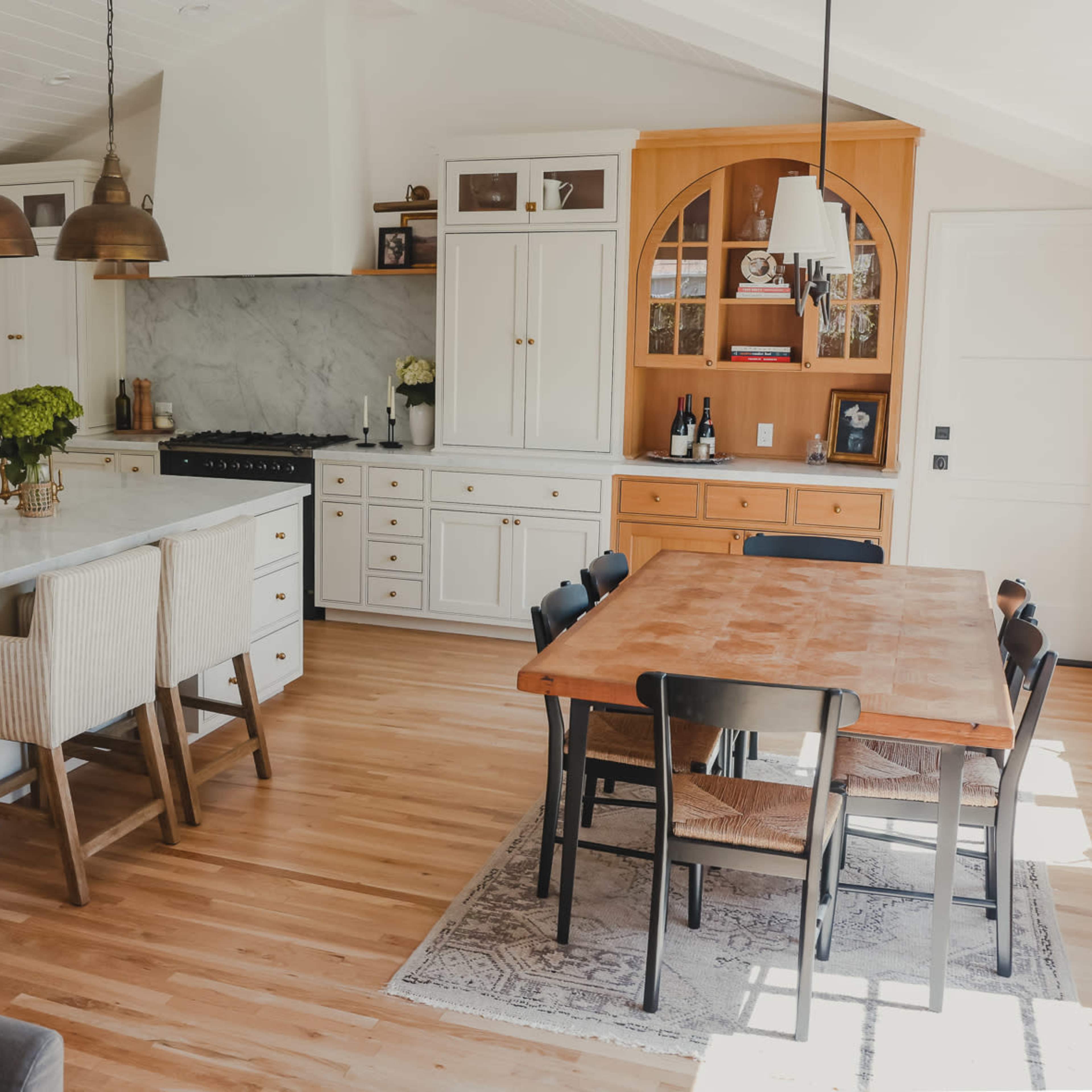 A modern kitchen featuring white cabinetry, a large marble island with seating, and a wooden dining table.