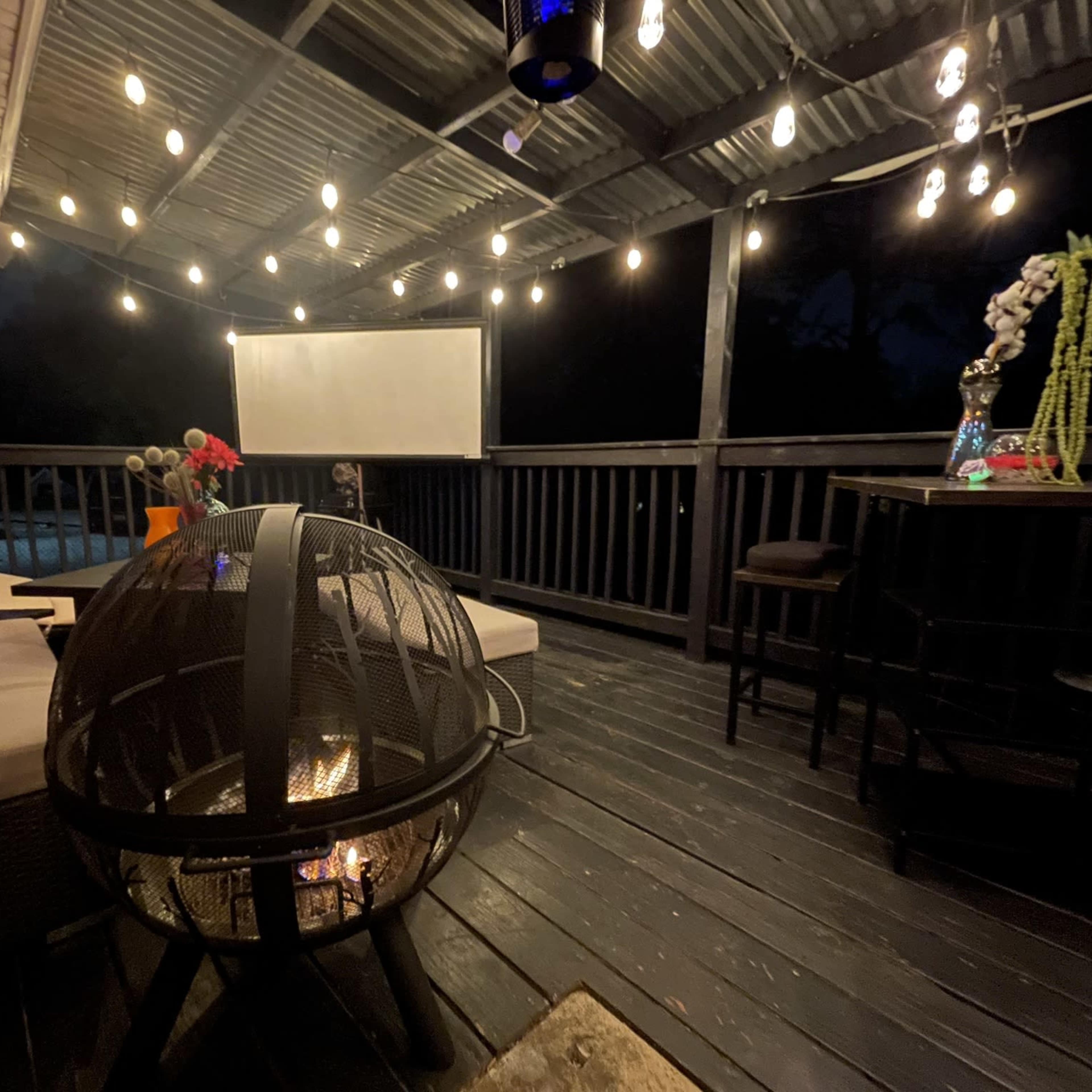 A cozy patio area features a spherical fire pit, comfortable seating, and string lights illuminating the space at night.