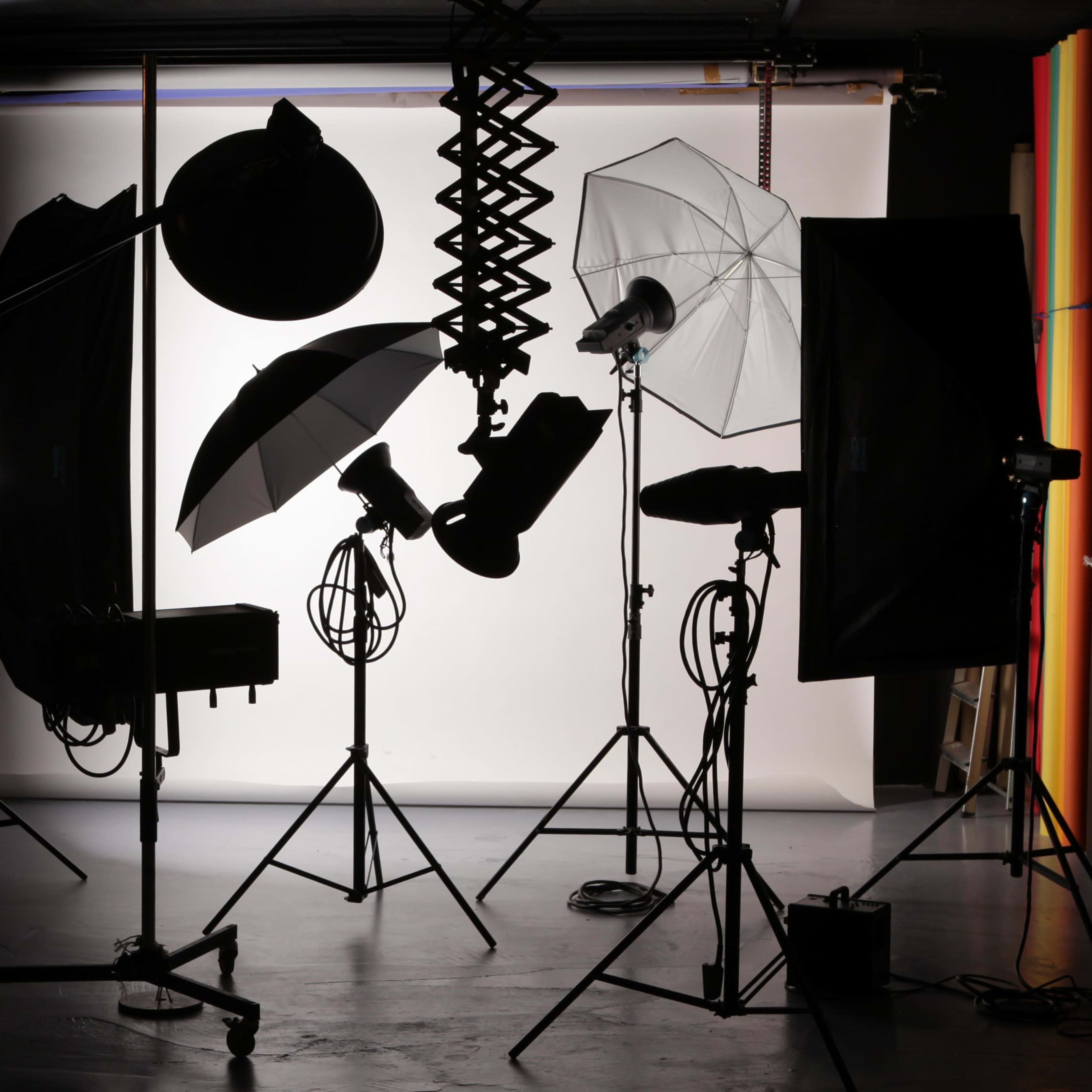 A photography studio setup with various lights and equipment silhouetted against a white backdrop.