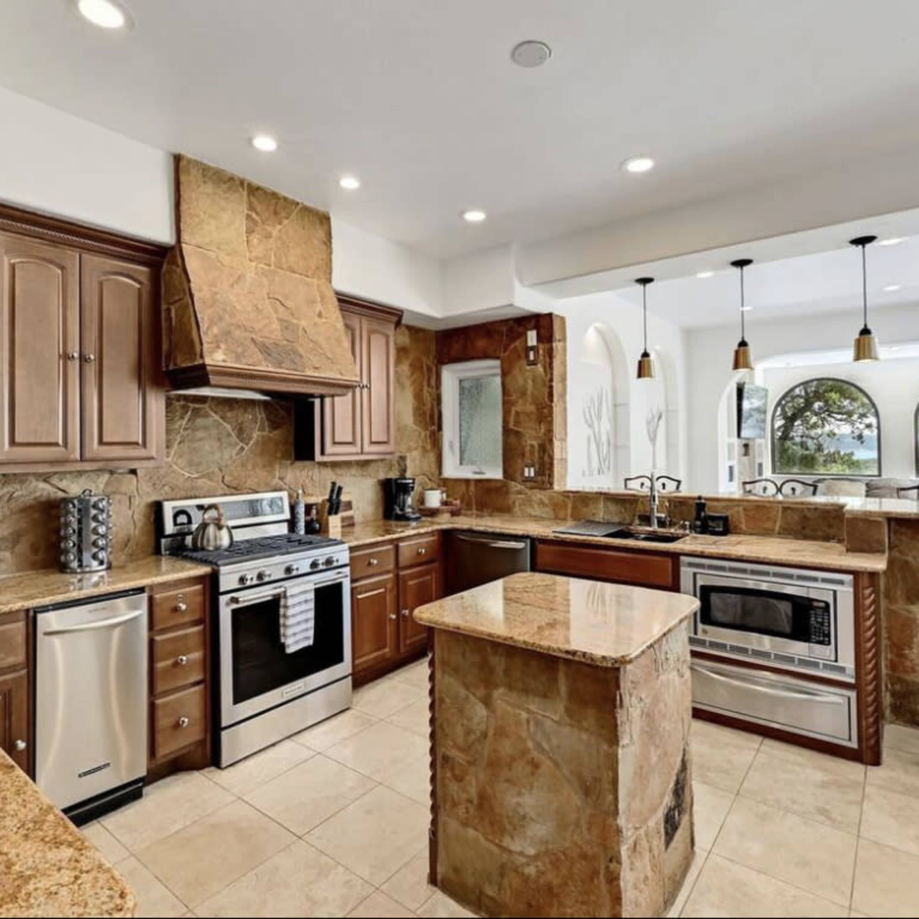 The kitchen features stone countertops and cabinetry, stainless steel appliances, and large windows overlooking a scenic view.