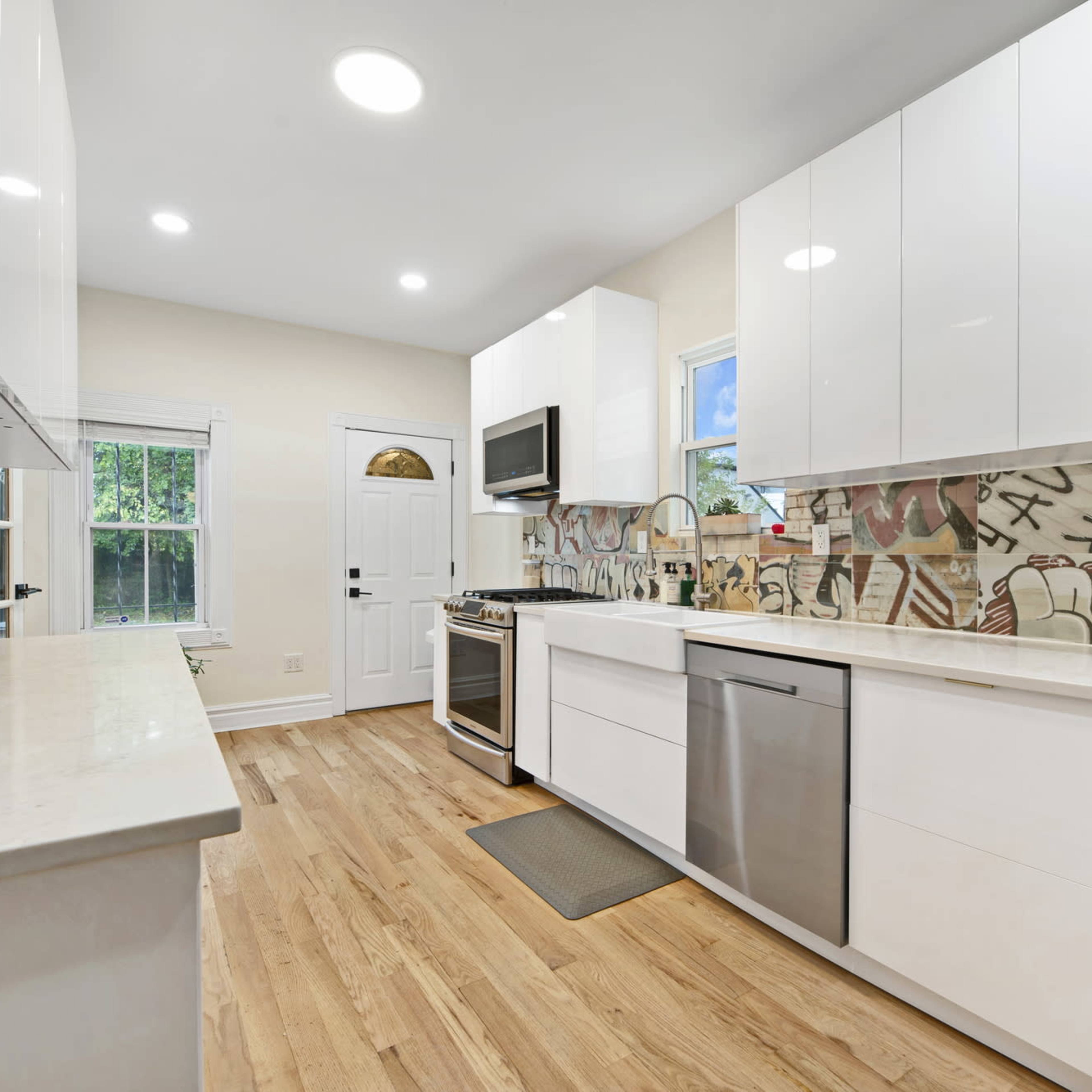 A modern kitchen features white cabinetry, stainless steel appliances, and a tiled backsplash with abstract designs.