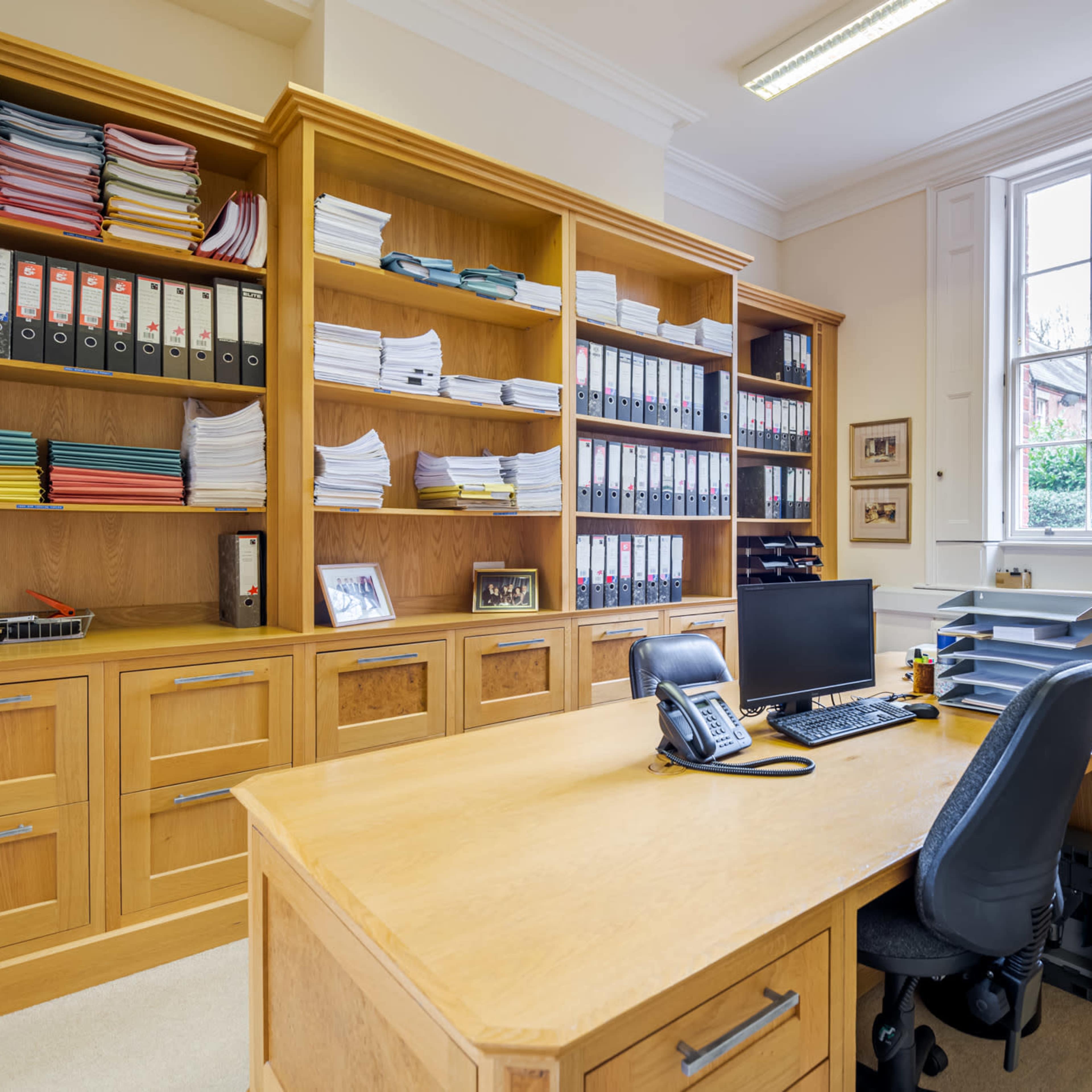 A wooden office with a desk, a computer, a phone, and shelves filled with neatly organized files and paperwork.